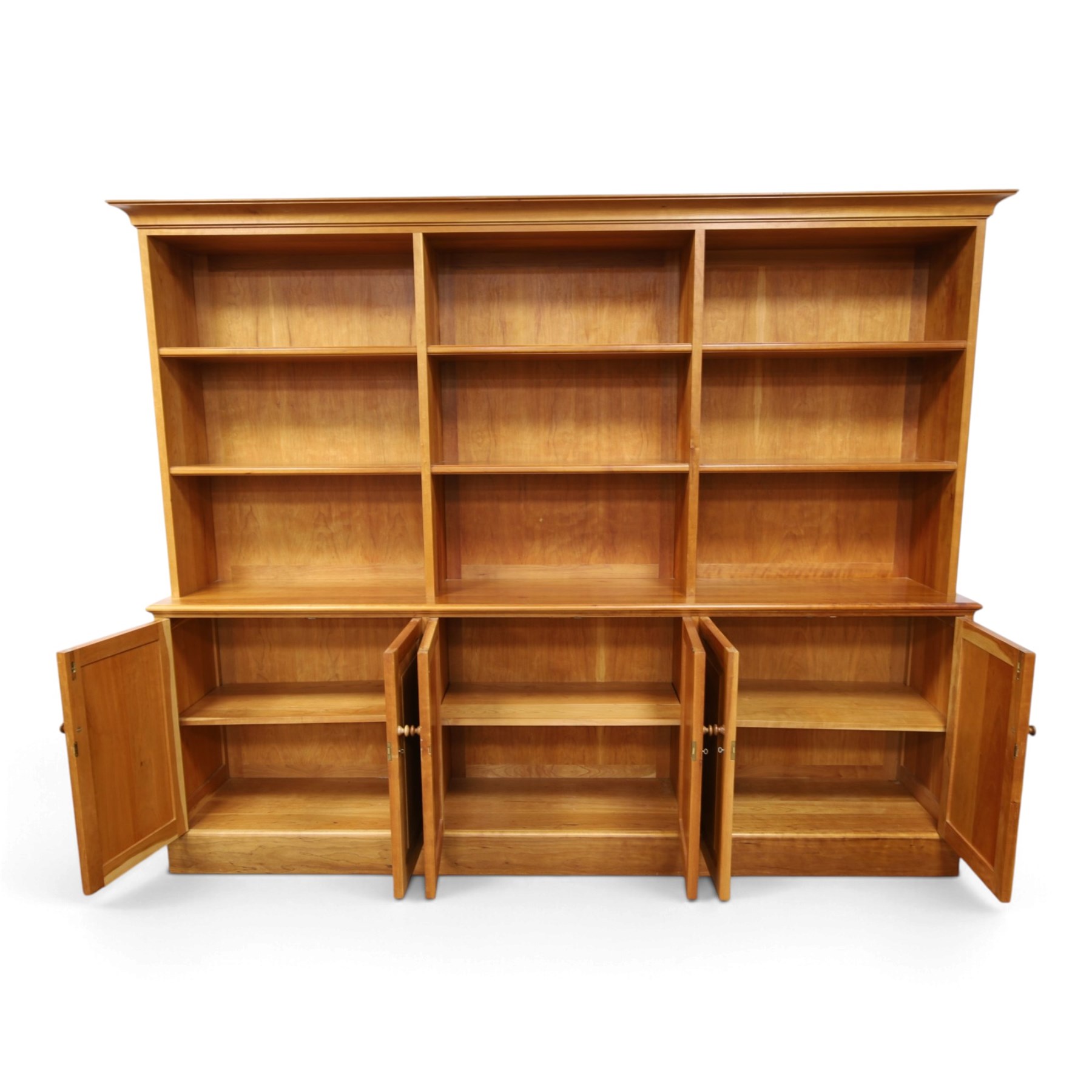 Philip Koomen (1953-) - Craftsman-made modern cherrywood large open
bookcase with a cupboard base, upper section with a
shaped cornice above three sections with two open
shelves, the lower section has three cupboards,
each with two panelled doors enclosing a single
shelf, raised on a plinth base
