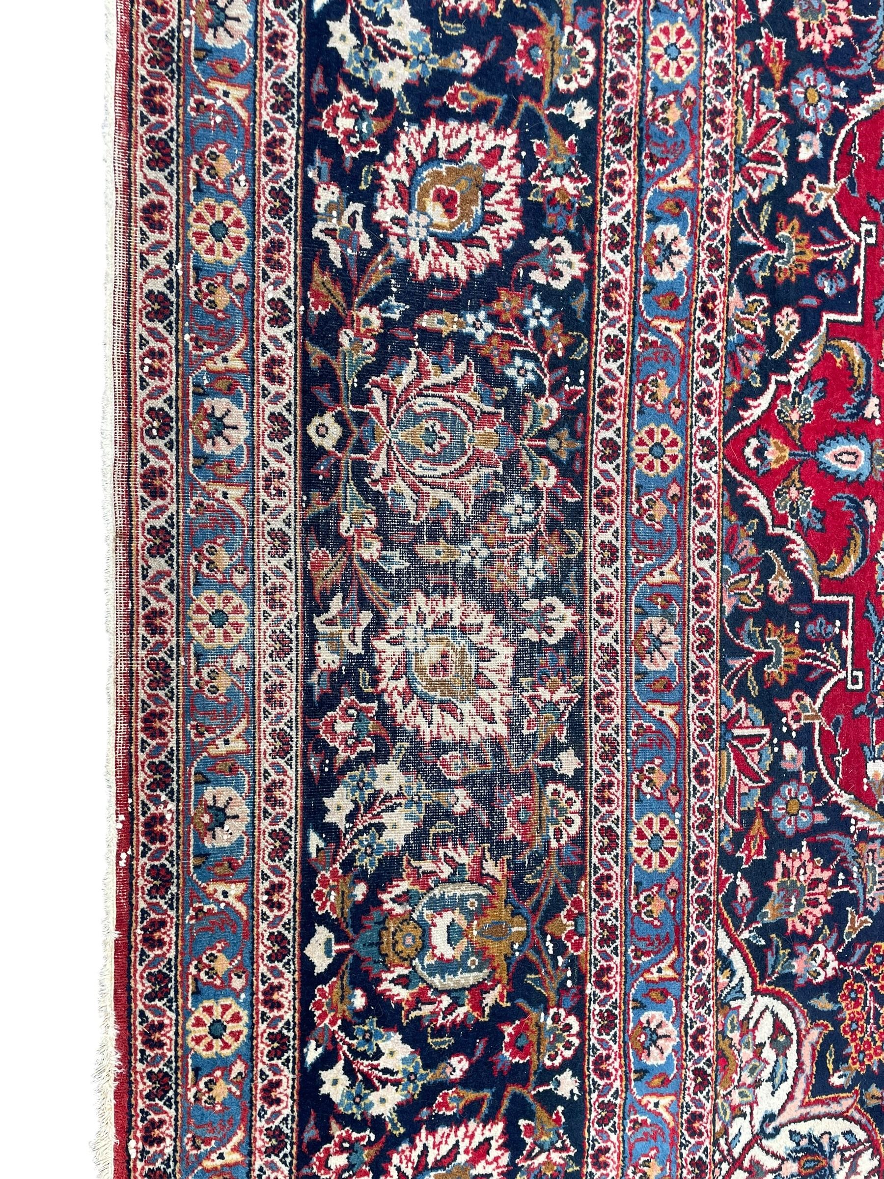 Large Persian Kashan crimson ground carpet, central floral medallion surrounded by swirling leafy branches and palmettes, enclose by floral pattern spandrels, the indigo border with overall scrolling design decorated with palmettes, within guard stripes 