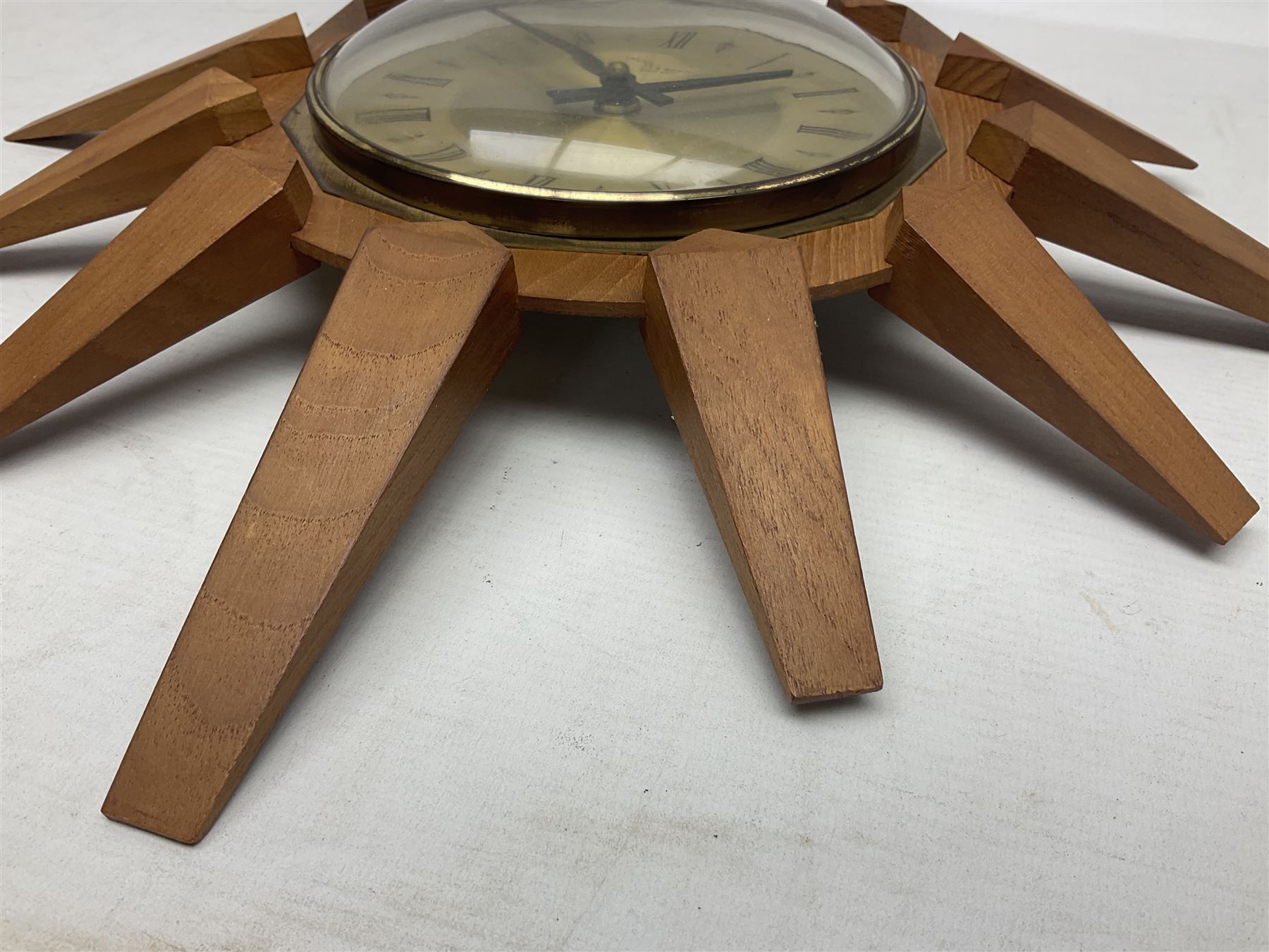 Mid-century teak sunburst wall clock by Anstey & Wilson, modelled with angular teak rays spreading from circular mount with plain brass face with Roman numerals, with battery operated Japanese movement, D45cm