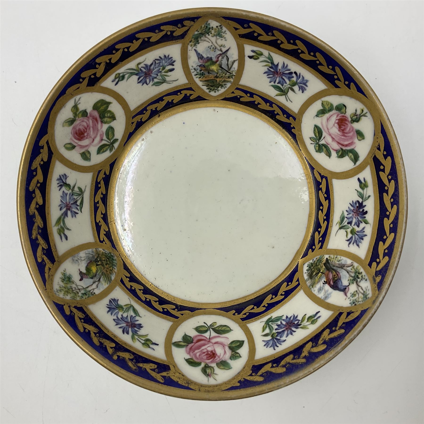 19th Sèvres style porcelain cup and saucer, the cup painted with a figural scene, against a scalloped border of scrolling floral swags on a blue ground, together with a Sèvres soft paste porcelain coffee can and saucer, painted with panels of exotic birds, roses and a border of cornflowers, LL monogram enclosing date letters H above painters mark, coffee can H6.5cm, saucer D13.5cm (2)