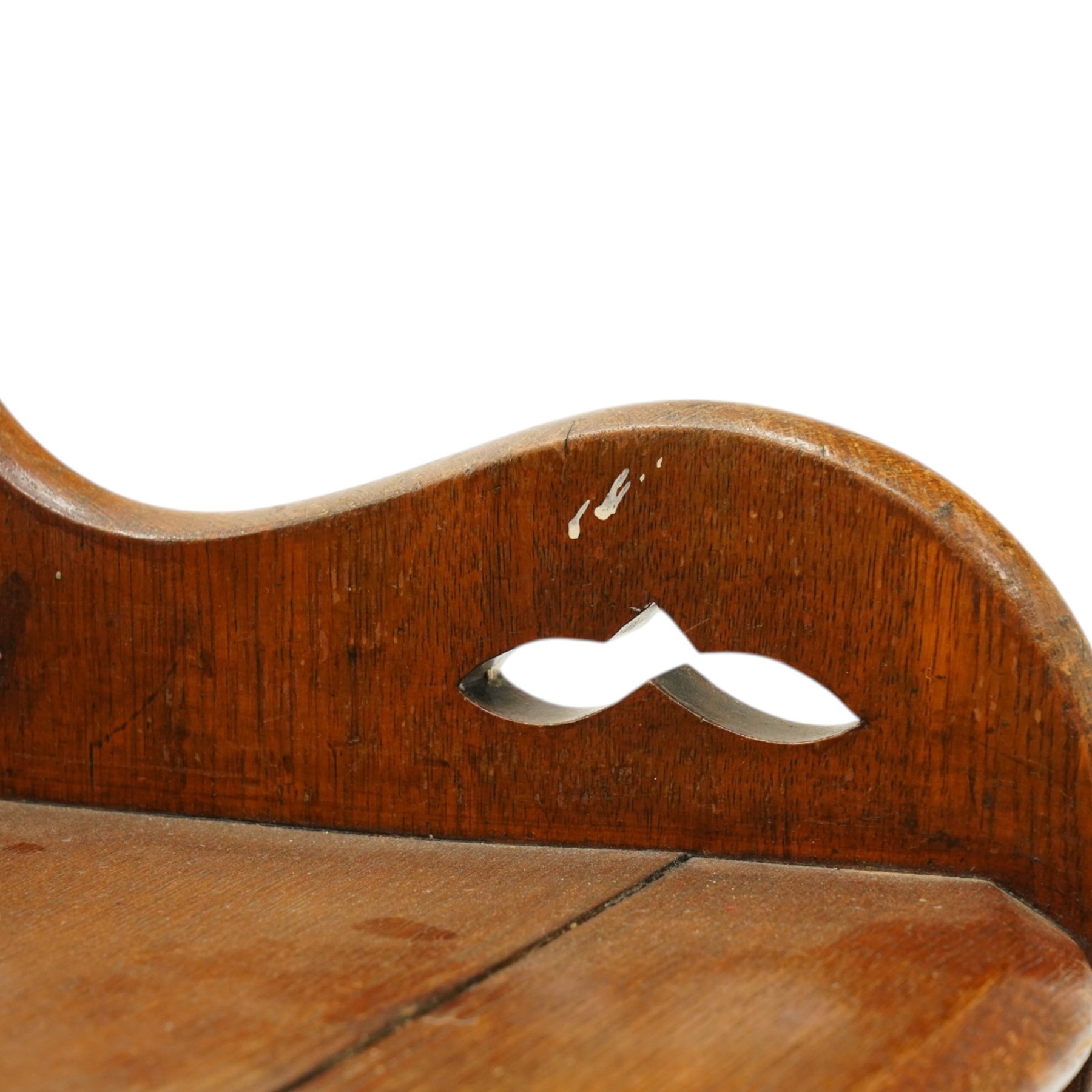 Late 19th century Gothic Revival carved oak hall chair or window seat, the swell-turned top rail centred by an arched carrying handle, over shaped open arms and solid plank seat, with pierced and carved scrolling foliate fretwork side panels and apron with applied central roundel, raised on shaped supports united by turned stretcher