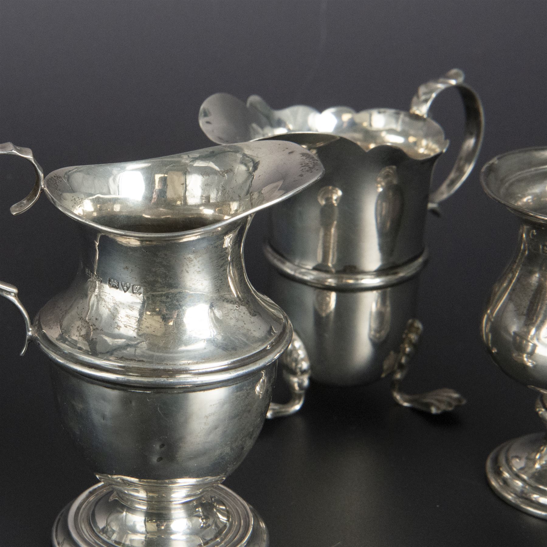 Group of early 20th century silver, comprising sauce boat, with flying scroll handle and upon three pad feet, two small cream jugs and a christening mug, all hallmarked, tallest H10cm