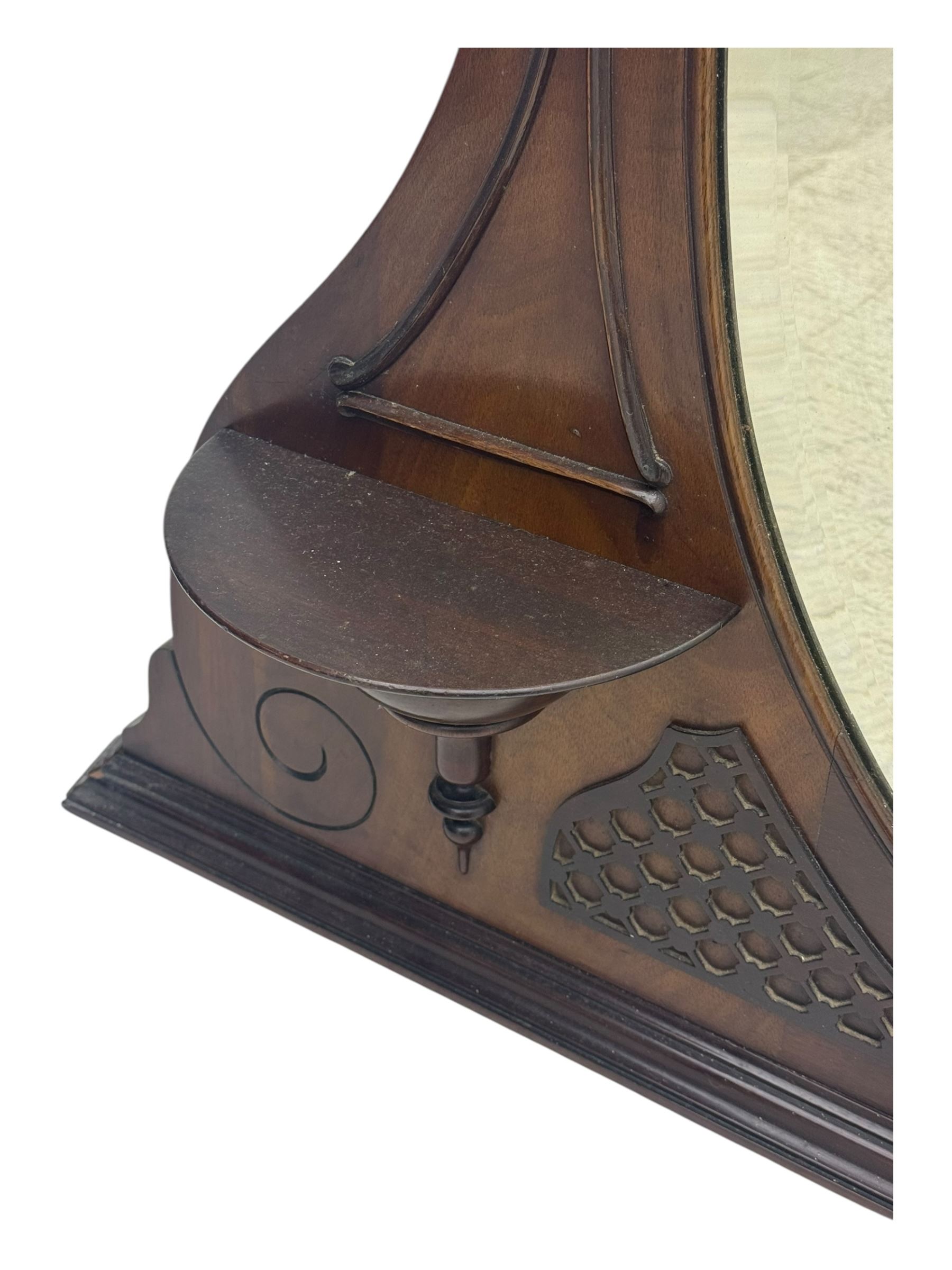 Early 20th century mahogany overmantel mirror, shaped broken pediment crest with open lattice panels, oval mirror plate flanked by scroll-carved bracket shelves

