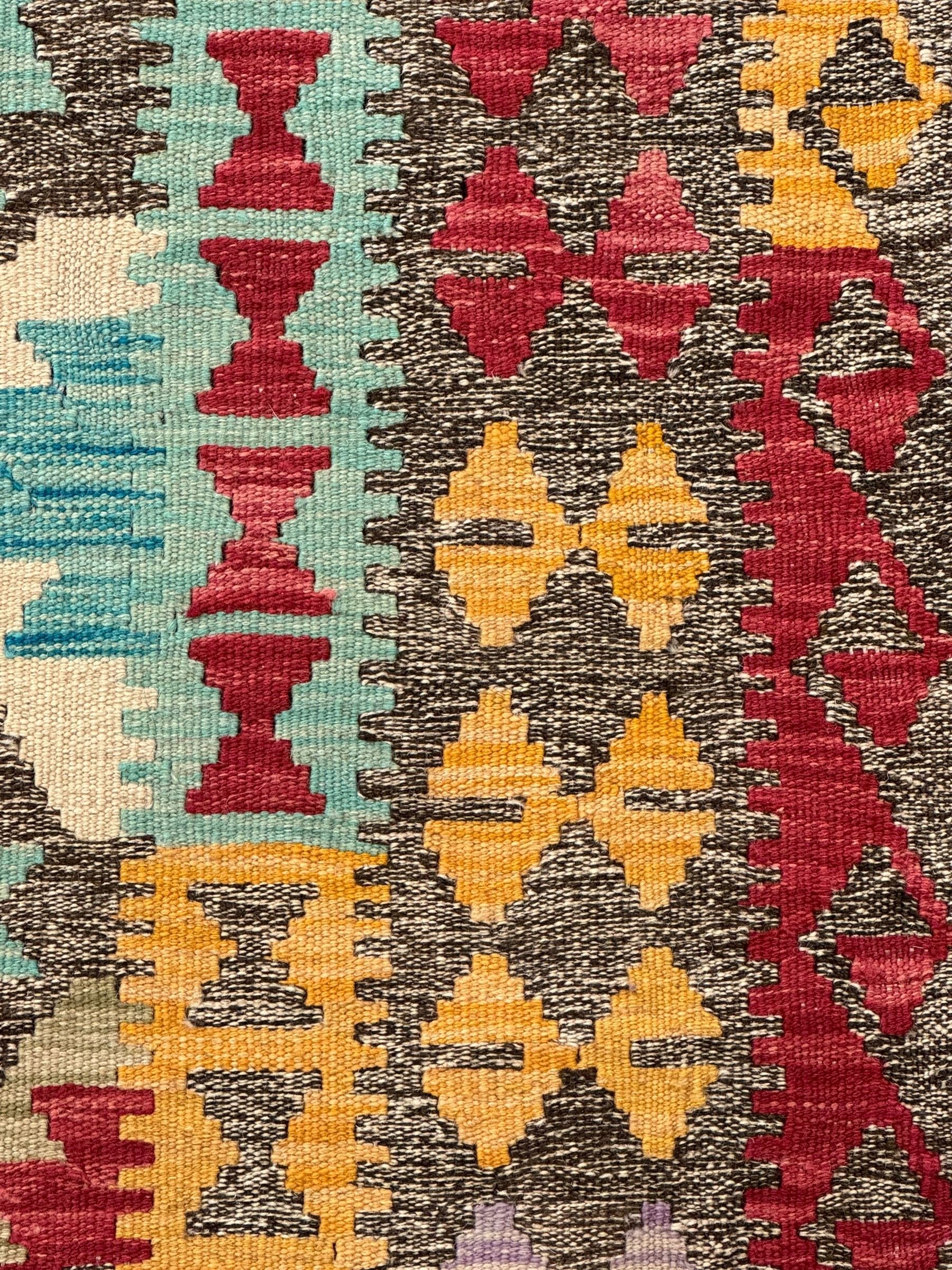 Anatolian Kilim cream ground rug, decorated with repeating diamond motifs in red, blue, yellow, and green, bordered by narrow bands of stylised geometric patterns in contrasting shades