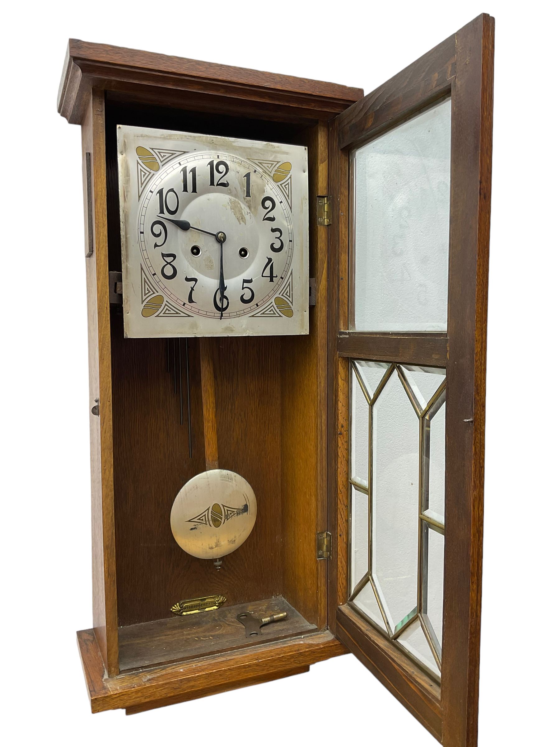 German - Art Deco oak cased 8-day wall clock c 1930, with a moulded flat top and fully glazed door, deeply cut bevelled glass panels and visible pendulum, silvered dial with Art Deco design spandrels, Arabic numerals, minute track and spade hands, twin train movement striking the hours and half hours on four gong rods. With pendulum and key.  