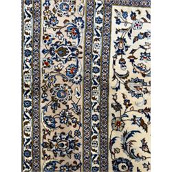 Central Persian Kashan hand-knotted carpet, ivory field with an all-over design of scrolling vines, lotus palmettes, and rosettes in shades of blue and brown within a blue ground border of palmettes and arabesques between multiple guard stripes, 
348 cm x 246cm