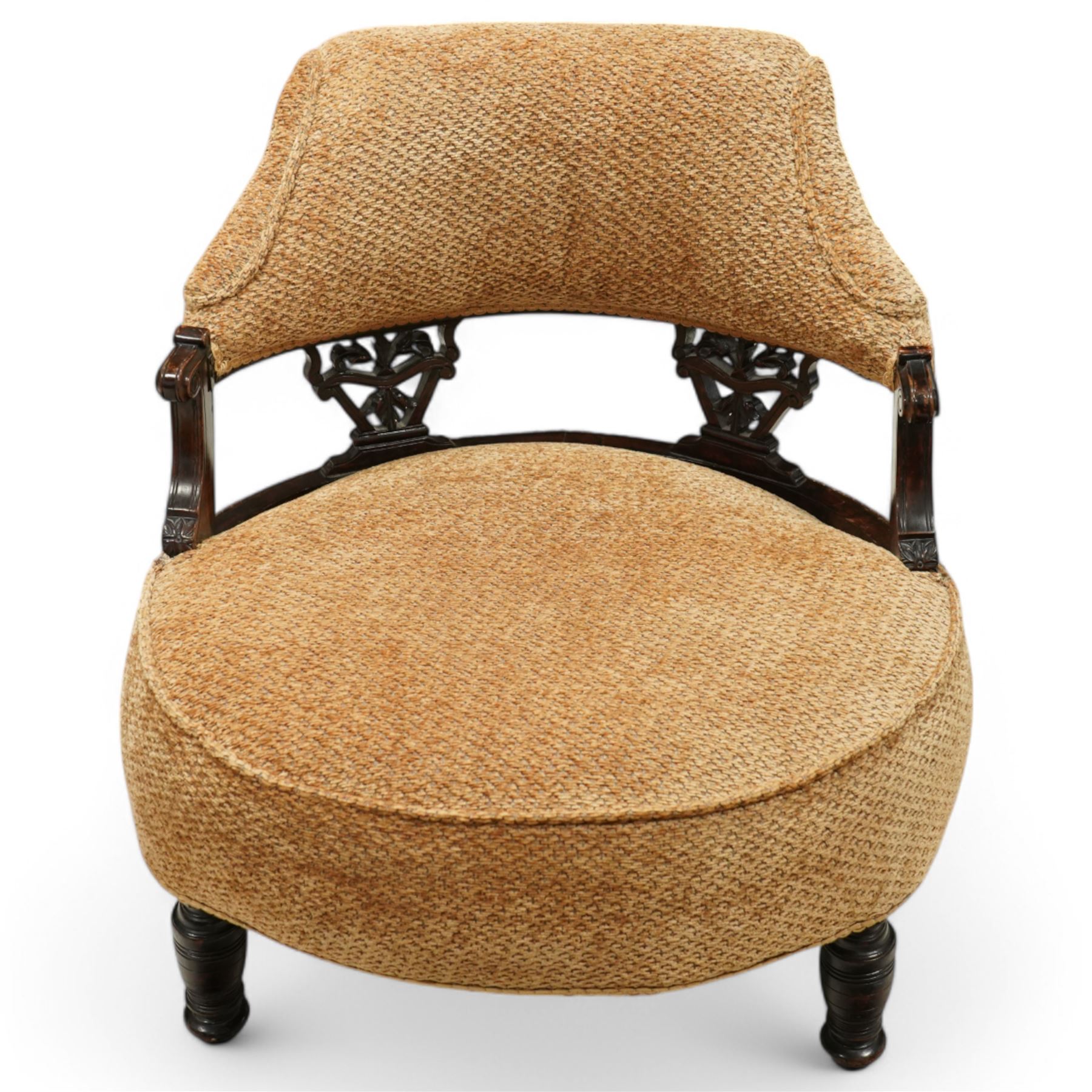 Late Victorian mahogany framed tub shaped chair, curved padded back and overstuffed seat in textured ochre fabric, pierced mahogany back supports with foliate and scroll carving, on turned front legs