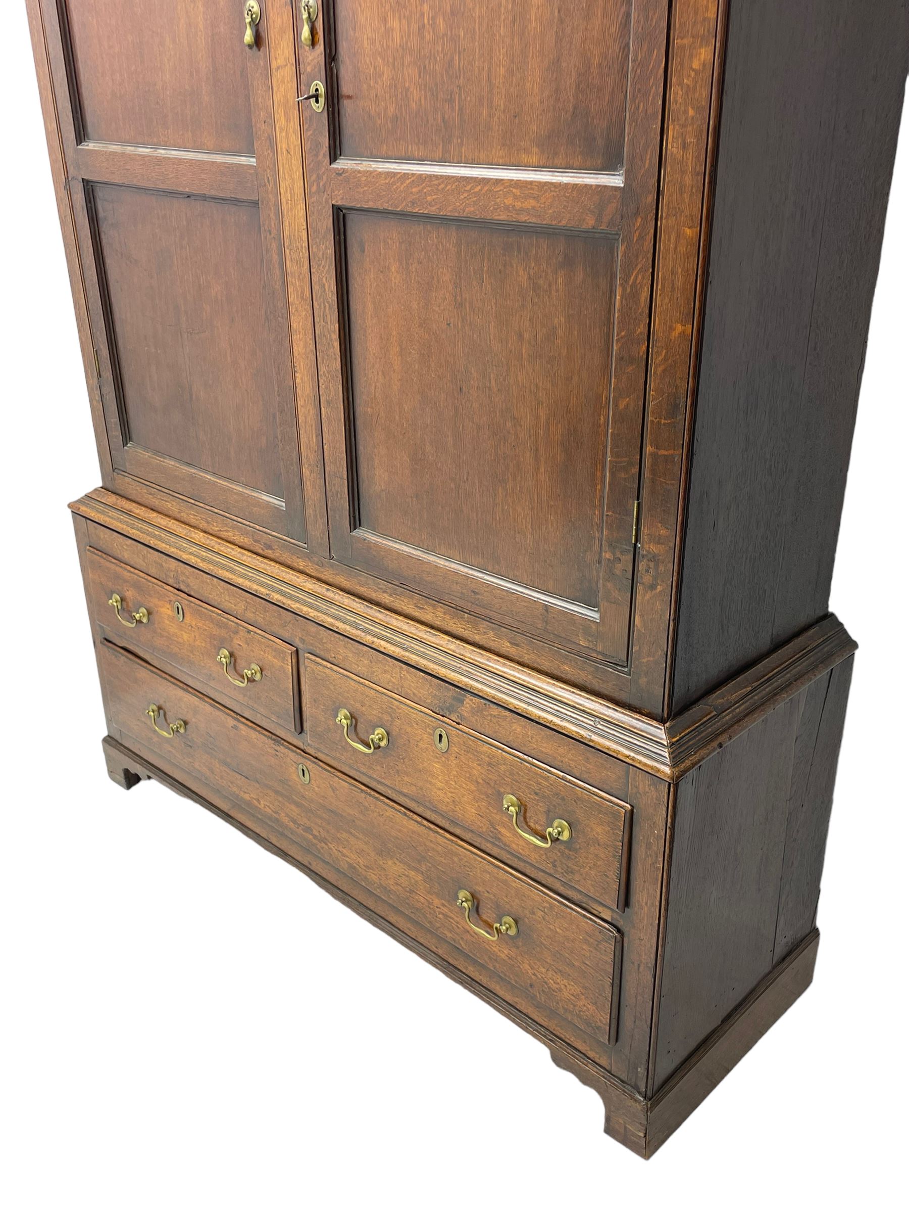 George III oak livery cupboard, projecting moulded cornice over two panelled doors, the upper panels within stepped ogee and arched moulded frame, the interior fitted with a single row of wooden hooks, two short and one long drawers, on bracket and return skirted base 