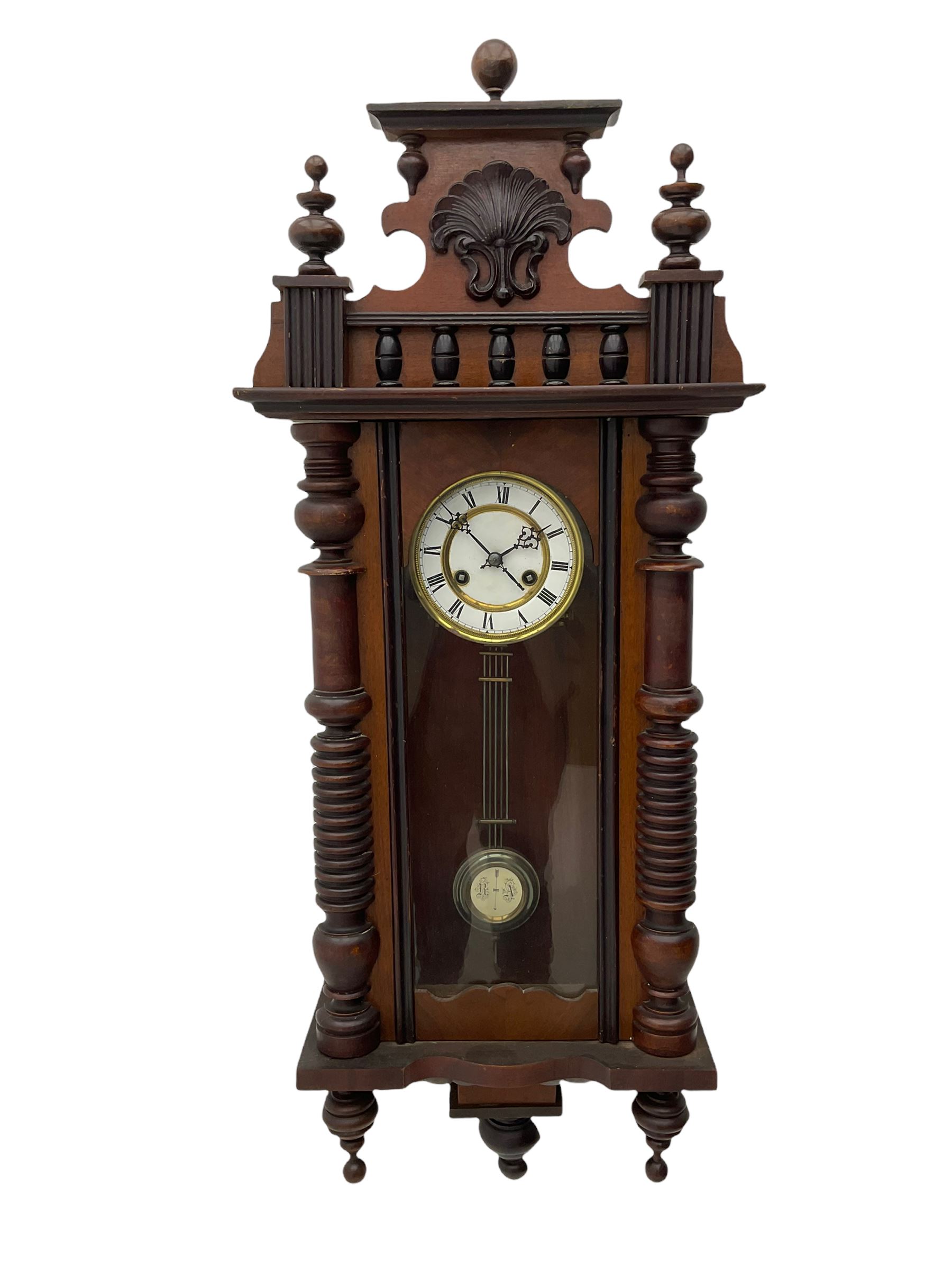A  German spring driven wall clock c1900 within a glazed case with side panels and a full-length arched door and ornately carved pediment, turned finials and original pendant finials, with a 5' two-piece white enamel dial with roman numerals, minute markers and pierced steel gothic hands, with a visible gridiron pendulum with an R/A inscribed pressed brass bob, eight-day movement striking the hours and half hours on a coiled gong.  



