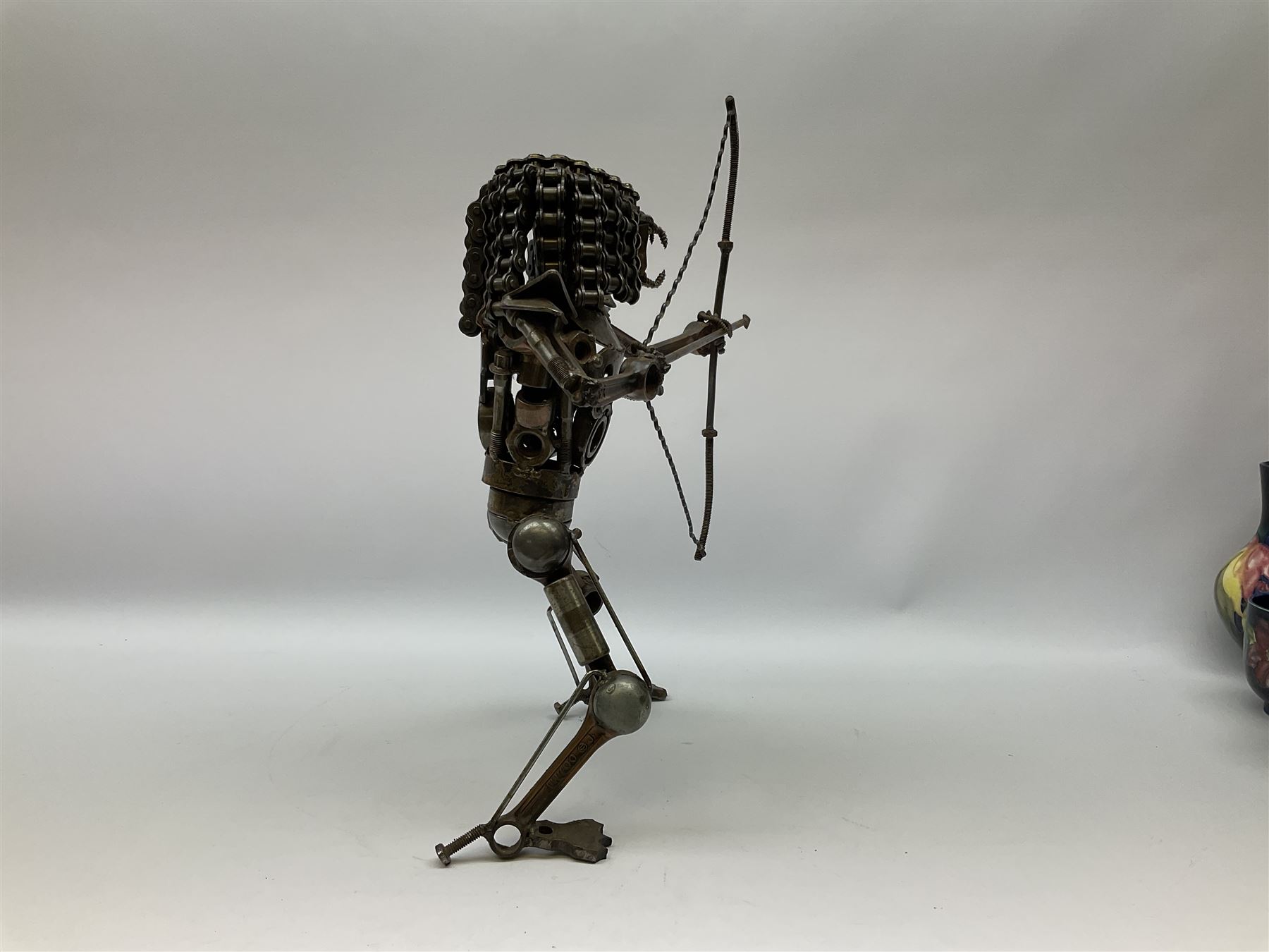 Predator metal sculpture, made with scrap metal, with articulated body, bike chain hair, and bow and arrow, H45cm