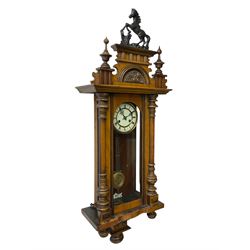 19th century 8-day German Vienna style wall clock, in a walnut case with a decorative pediment and turned finials, fully glazed door with a gridiron pendulum, white enamel two part dial with Roman numerals and pierced hands, twin train spring driven movement sounding the hours and half hours on a coiled gong.