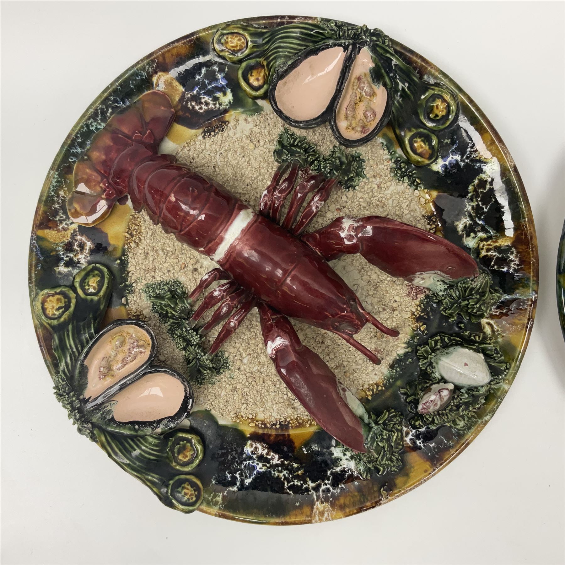 Two 20th Century Portuguese Palissy style Majolica wall plates, one depicting a crab, the other a lobster each to the centre modelled in relief surrounded by encrustations and shells, both with impress marks beneath, D32cm