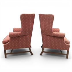 Georgian design wingback armchairs, the high backs flanked by shaped wings over padded scroll arms, upholstered in burgundy and gilt fleur-de-lys patterned fabric, loose cushion seats, raised on square tapering front supports