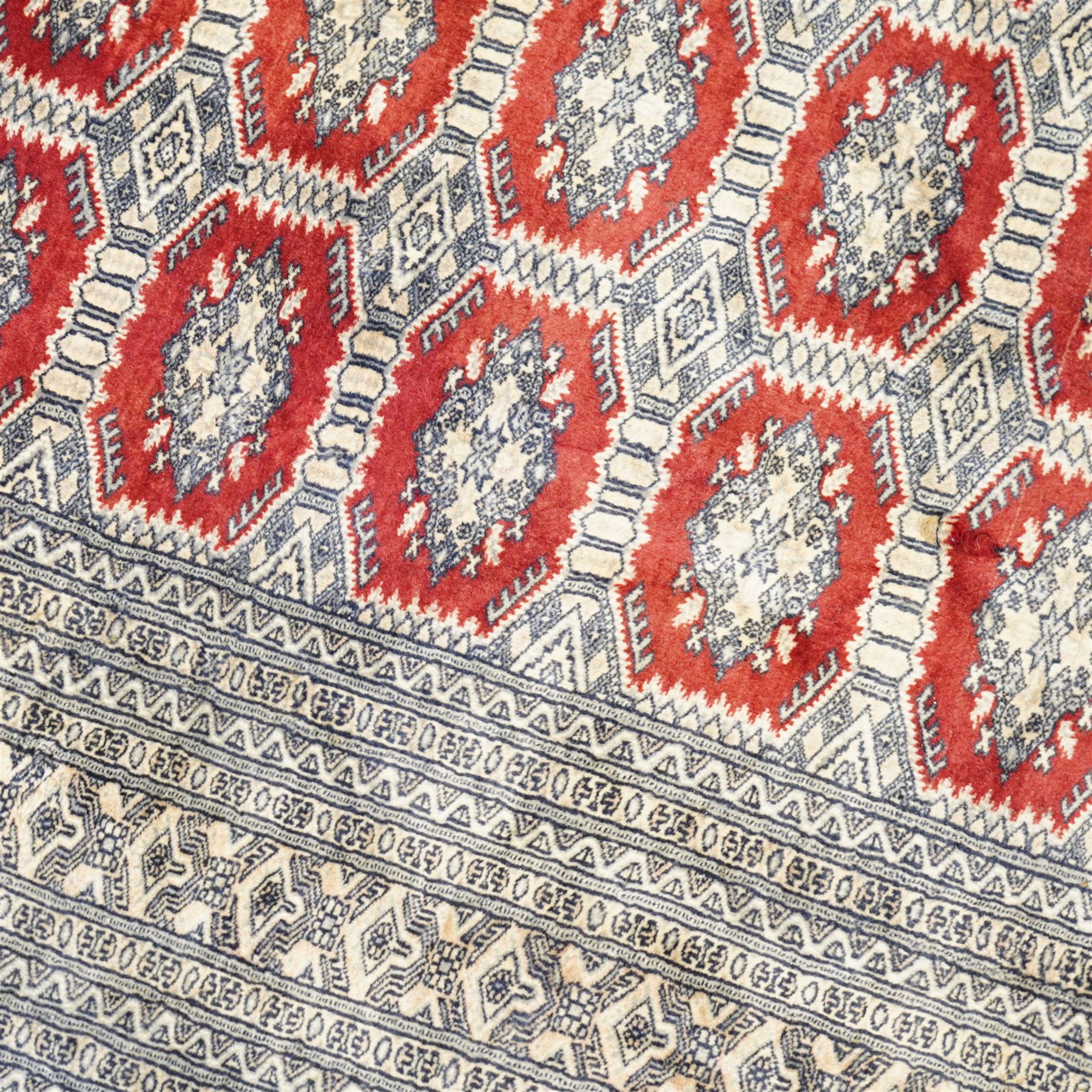 Jaldar Bokhara crimson and pale ground carpet, the field decorated with five rows of Gul motifs, within intricate multi-band border decorated with repeating geometric designs 