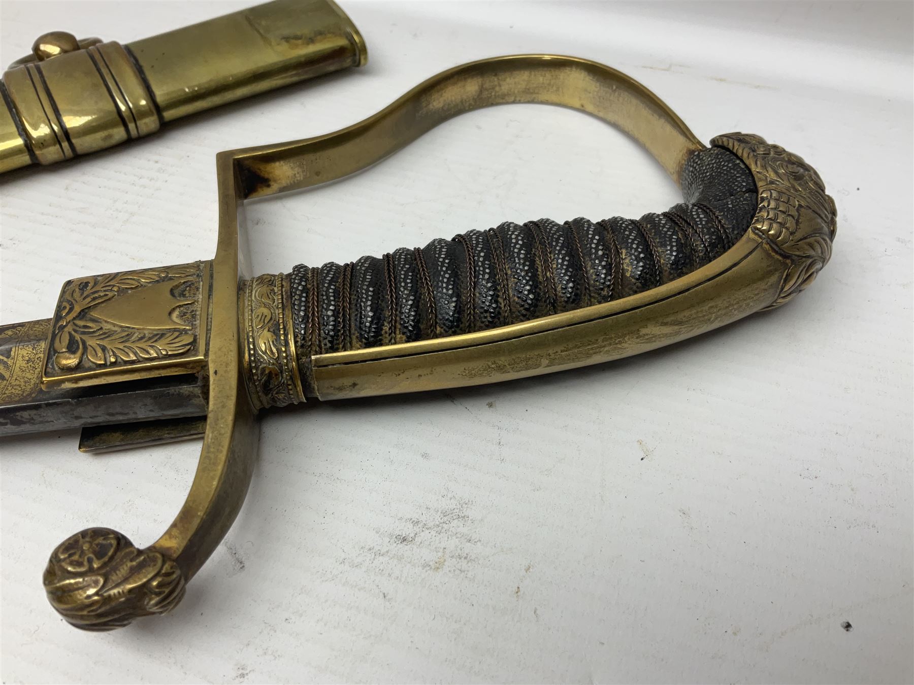 German Saxon 1st Empire Light Cavalry officer's sword c1820s, the 79cm clipped curving blade engraved with the crest of Hanover and various battle trophies with traces of blueing and gilding, brass hilt with knucklebow, foliate square langets, ornate downswept quillon, wire-bound fish skin grip with lion's head pommel; in brass scabbard with two suspension rings L95cm overall