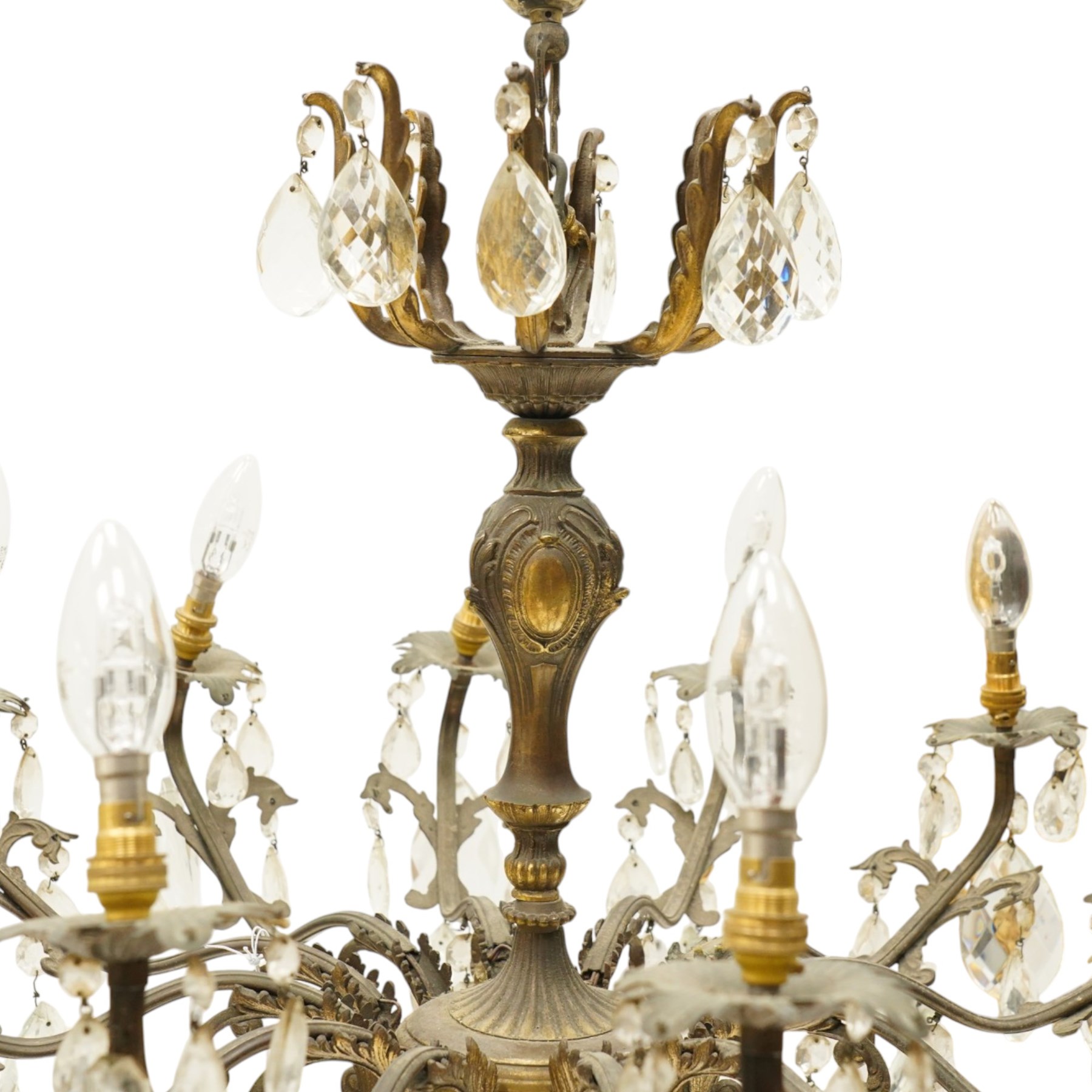 20th century Louis XV design gilt and patinated metal twelve-light chandelier, the foliate-cast baluster stem issuing scrolling acanthus branches with leaf-form drip pans, hung throughout with faceted glass pendants and lustre drops, suspended from chains beneath a foliate ceiling rose