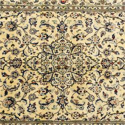 Central Persian Kashan hand-knotted rug, ivory ground, with a small central floral medallion and pendants, the field finely decorated with blue, cream and soft red scrolling vines, flowerheads and palmettes, within an ivory floral border and narrow guard stripes, with cotton fringes
