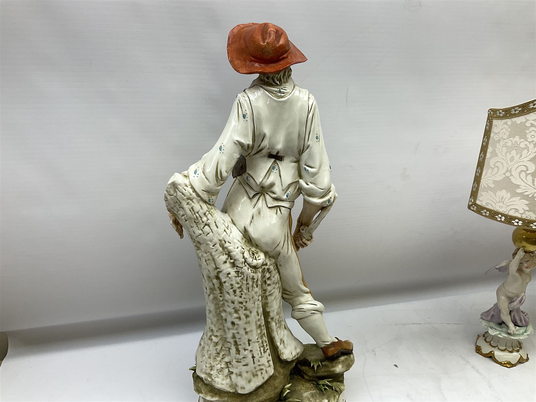 Pair of Capodimonte table lamps, in the form of cherubs holding a brass fitting, together with a pair of large Capodimonte figures in the form or a man and woman resting up on tree stump, largest example H57cm