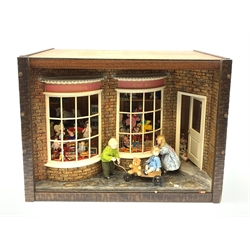 A 1/12th scale diorama of a toy shop window, depicting three children outside 'Adelaide's Toy Shop', the windows displaying assorted toys, including dolls, skittles, teddy bears, rocking horse, dolls house, etc. 

H29cm L40cm D26cm.