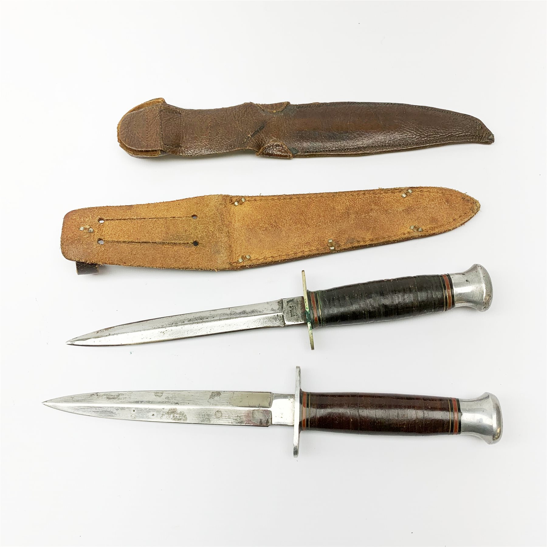 American WW2 type fighting knife the 15cm steel double edged blade marked to the ricasso William Rodgers Sheffield England, nickel crosspiece, leather bound grip and aluminium pommel L27cm overall; and another similar fighting knife with aluminium crosspiece; both in leather sheath (2)
