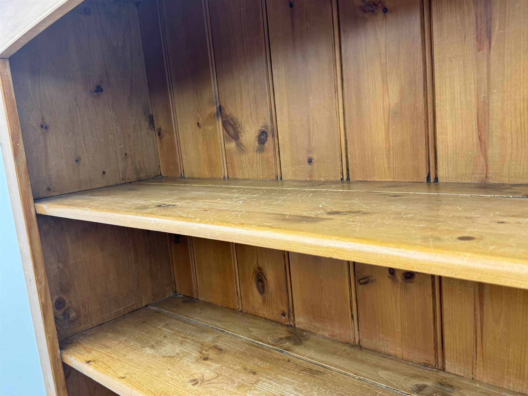 Early 20th century pine kitchen dresser, featuring a hutch with arched top over three open shelves, the base with five drawers over three cupboard doors, turned column supports flanking the doors, scalloped apron base with bracket feet