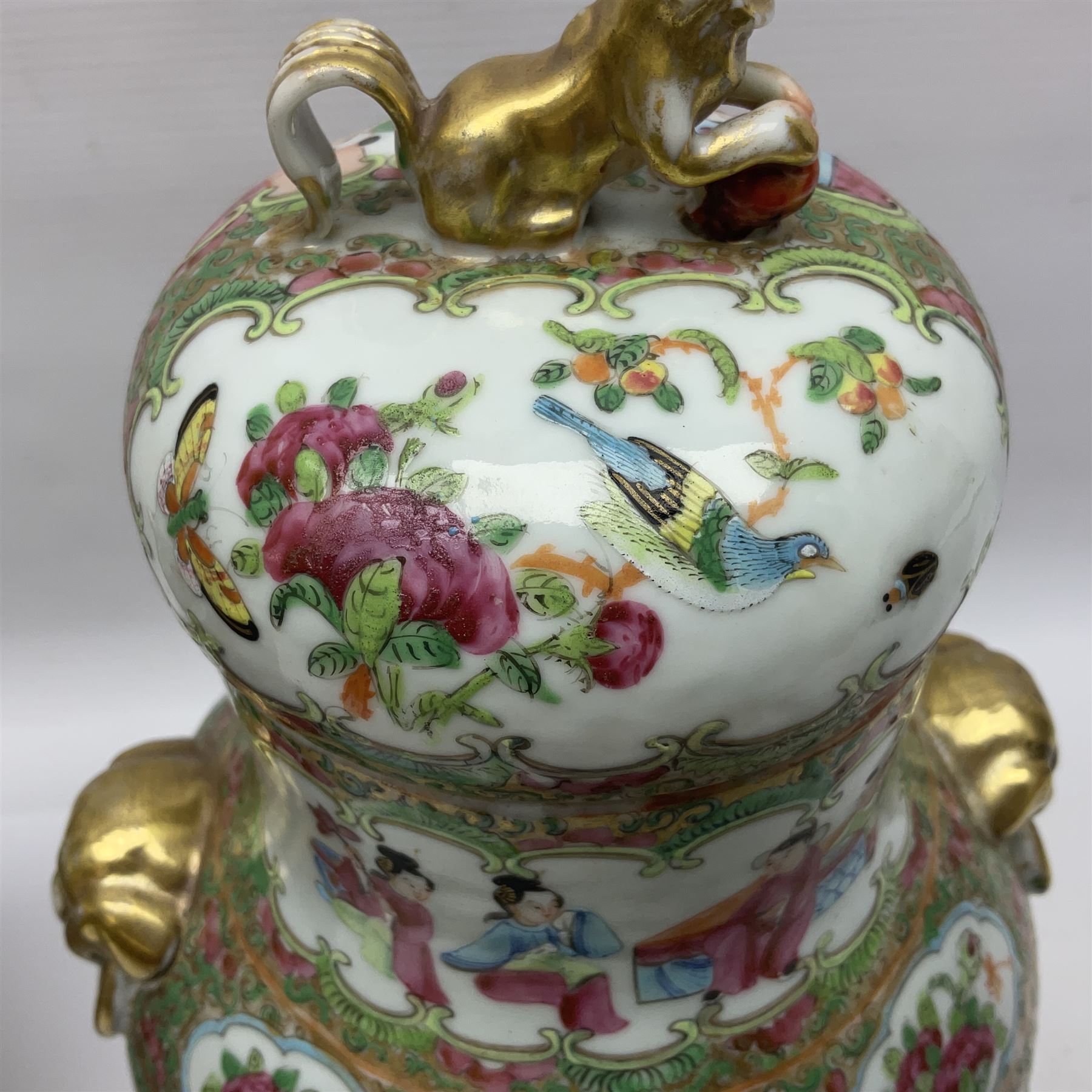 Pair of 19th century Chinese Famille Rose vases and covers, each of baluster form with twin gilt lion mask ring handles to shoulders, the flattened domed covers with gilt temple lion finials, each decorated with alternating reserves of bijin and attendants, and birds and butterflies amongst blossoming peonies, against a gilt ground profusely decorated with stylised scrolls, H32.5cm