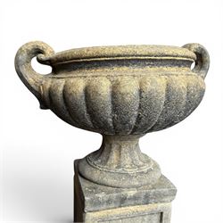 Pair of Neoclassical design weathered cast stone garden urns of kylix form, the rolled rim flanked by twin pierced scroll handles over a shallow gadrooned bowl, raised on a fluted circular socle and faux panelled square pedestal base