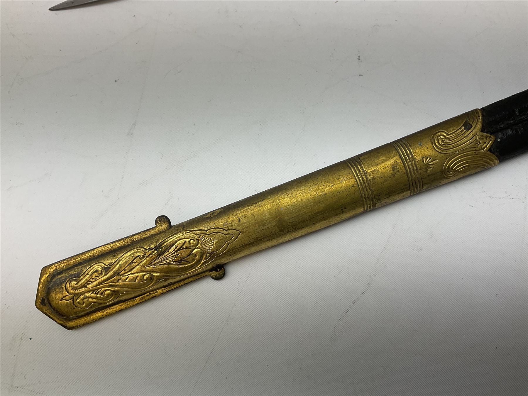 WW1 George V era 1827 Pattern Royal Naval Officer’s sword, the 80cm fullered steel blade decorated with crown, fouled anchor etc and marked Gieves Portsmouth London Edinburgh Devonport to the ricasso, gilded hilt with fouled anchor and crown, wire-bound ray skin grip, lion’s head pommel with mane backstrap, folding/locking langet and full bullion knot; in  leather scabbard having twin brass lockets with hand engraved panels and twin suspension rings L94cm overall. Provenance: By direct family descent from Brian Heathcote HMS Conqueror later Superintendant in the Liverpool Special Constabulary.