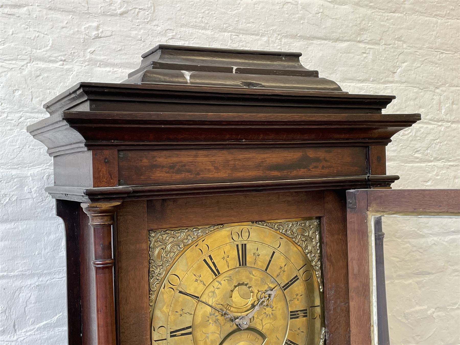 18th century c1760 oak cased George III longcase clock by William Eastwood of Burnley, with a stepped caddy top on a projecting cornice and blind frieze, square glazed door flanked by two turned pillars with gesso capitals, trunk with conforming recessed pillars and a full length wavy topped door, on a square plinth with a raised panel and shaped skirting, 12” square brass dial, 11” chapter ring with Roman numerals and five-minute Arabic's,  