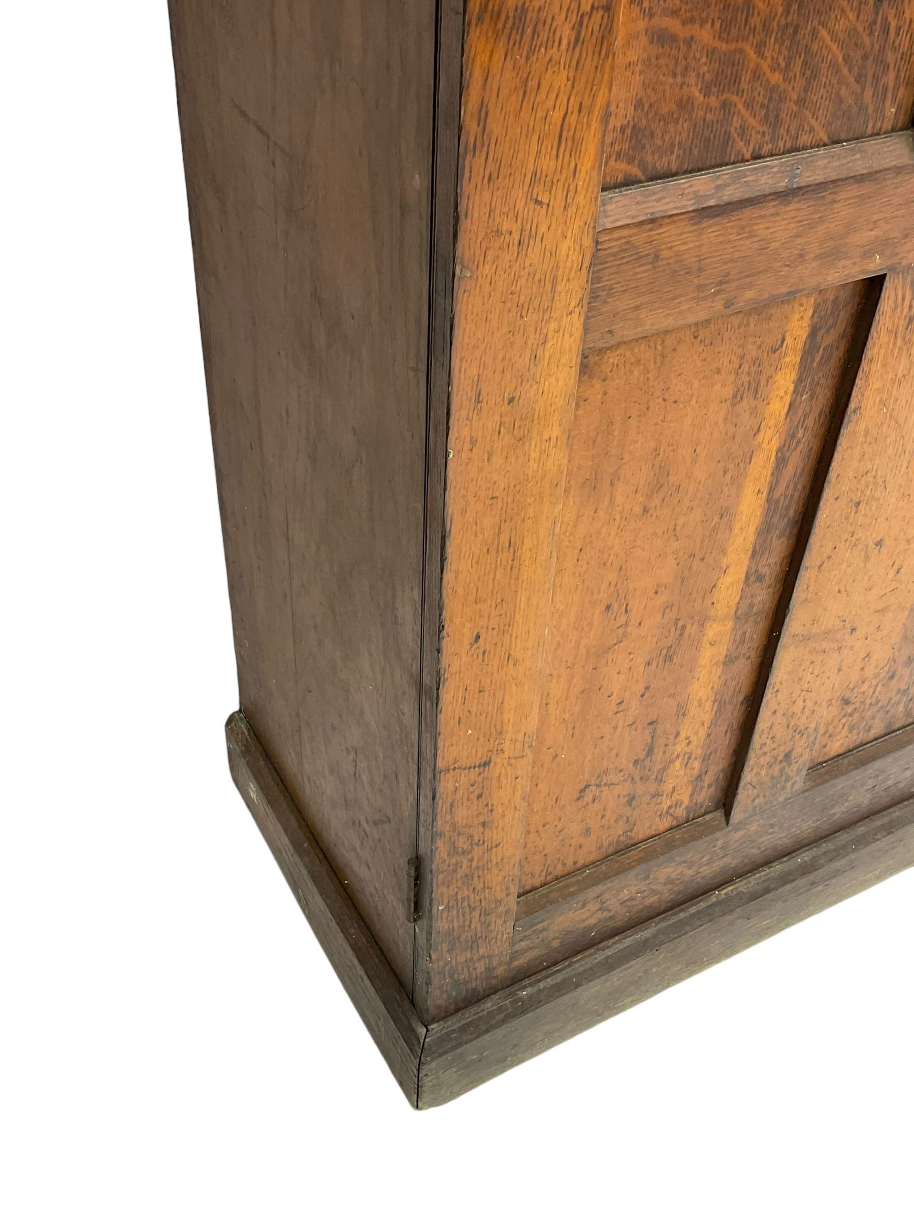 The North of England School Furnishing Company Limited Darlington - early 20th century oak school cupboard, projecting moulded cornice over two panelled doors, fitted with shelves, on chamfered plinth base 