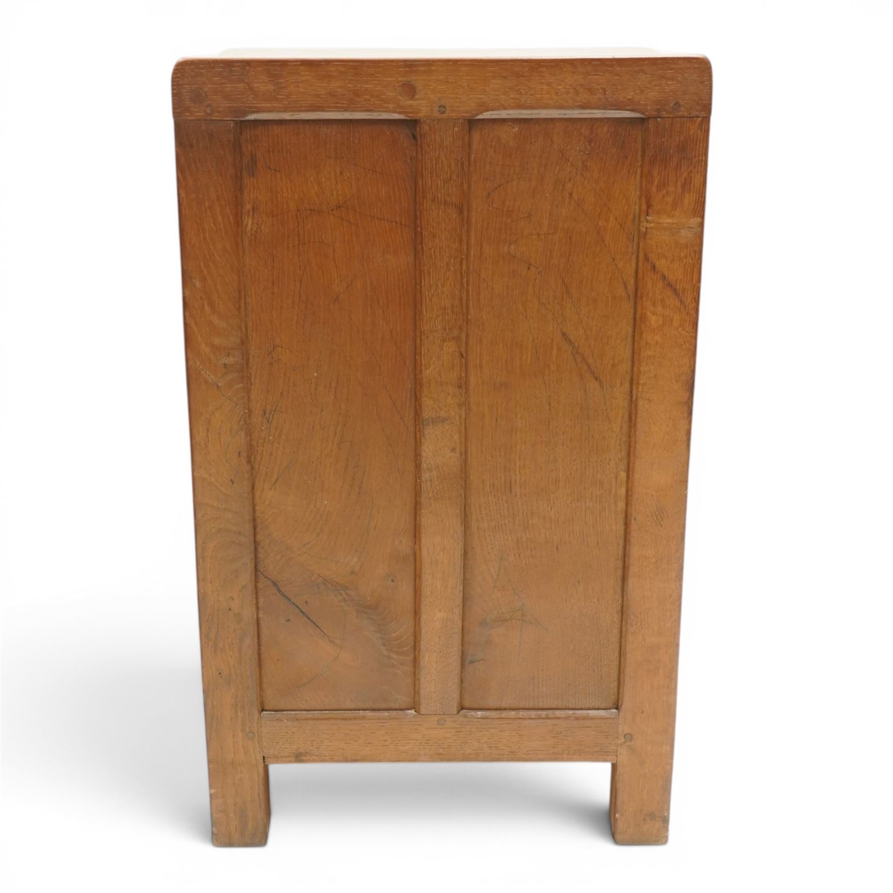 Mouseman - early-to-mid-20th century adzed and panelled dark oak bedside cupboard, raised back over rectangular canted top, fitted with single panelled cupboard door with chamfered rails and wrought iron fittings, enclosing two adjustable shelves, raised on canted square feet, carved with mouse signature, by the workshop of Robert Thompson of Kilburn