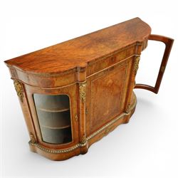 Late Victorian figured walnut credenza, the shaped demi-lune top with cross-banding and stringing over an inlaid frieze with foliate gilt-metal mounts, fitted with a central geometric-inlaid panelled door, flanked by convex-glazed side-cabinets with a gilt metal slip and outer-banding, the uprights surmounted by gilt-metal cartouche mounts with cascading foliage details, raised on a shaped skirted base with central female-mask gilt mount