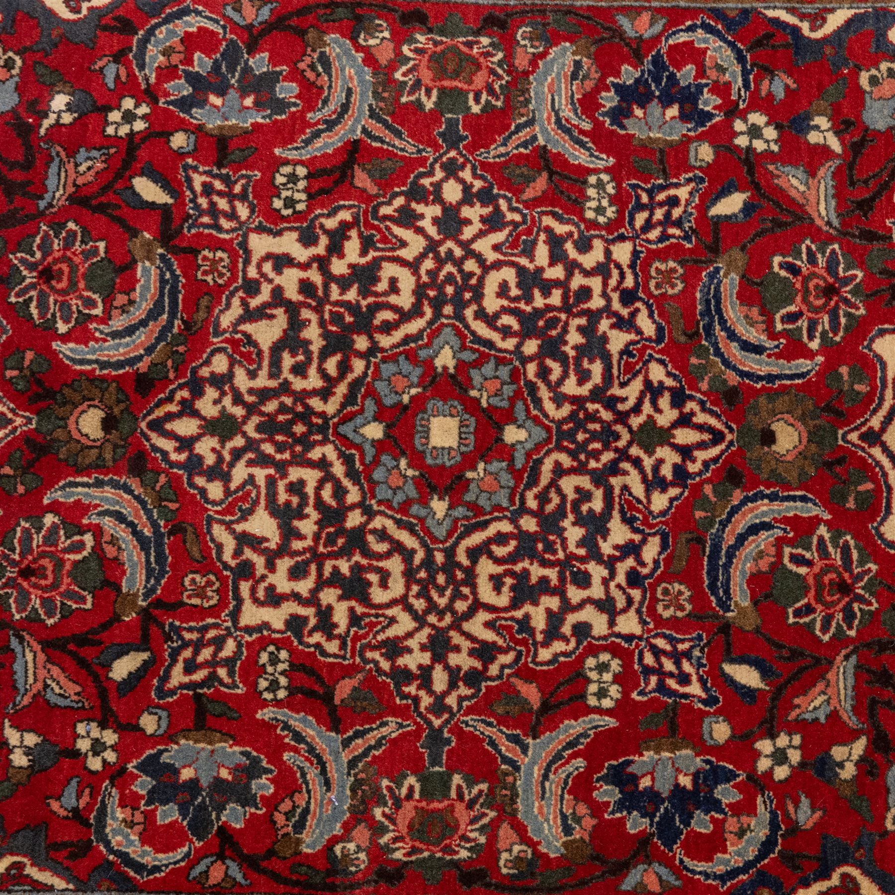 Central Persian Isfahan hand-knotted rug, madder red field, with elaborate central medallion with pendants and scrolling arabesques, palmettes and stylized floral sprays arranged in a densely ornamented ground of classical Safavid inspiration, ivory border with a continuous vine scroll of palmettes and rosettes, flanked by multiple guard stripes in navy and red with geometric and floral motifs, with cotton fringe ends 