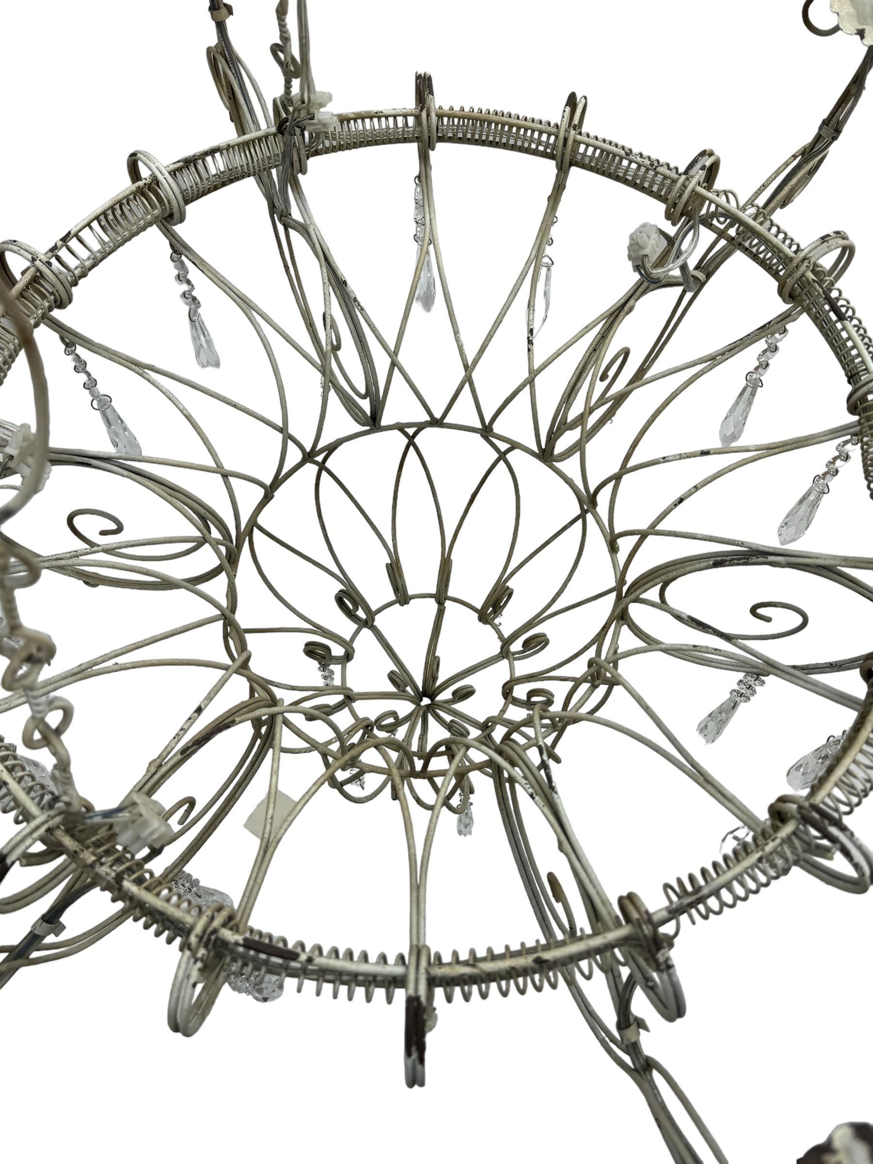 India Jane Interiors - six branch metal chandelier, the scrolled crown over circular bulbous body with six projecting branches, decorated with scroll work and glass pendants, in distressed white paint finish - ex-display/bankruptcy stock 