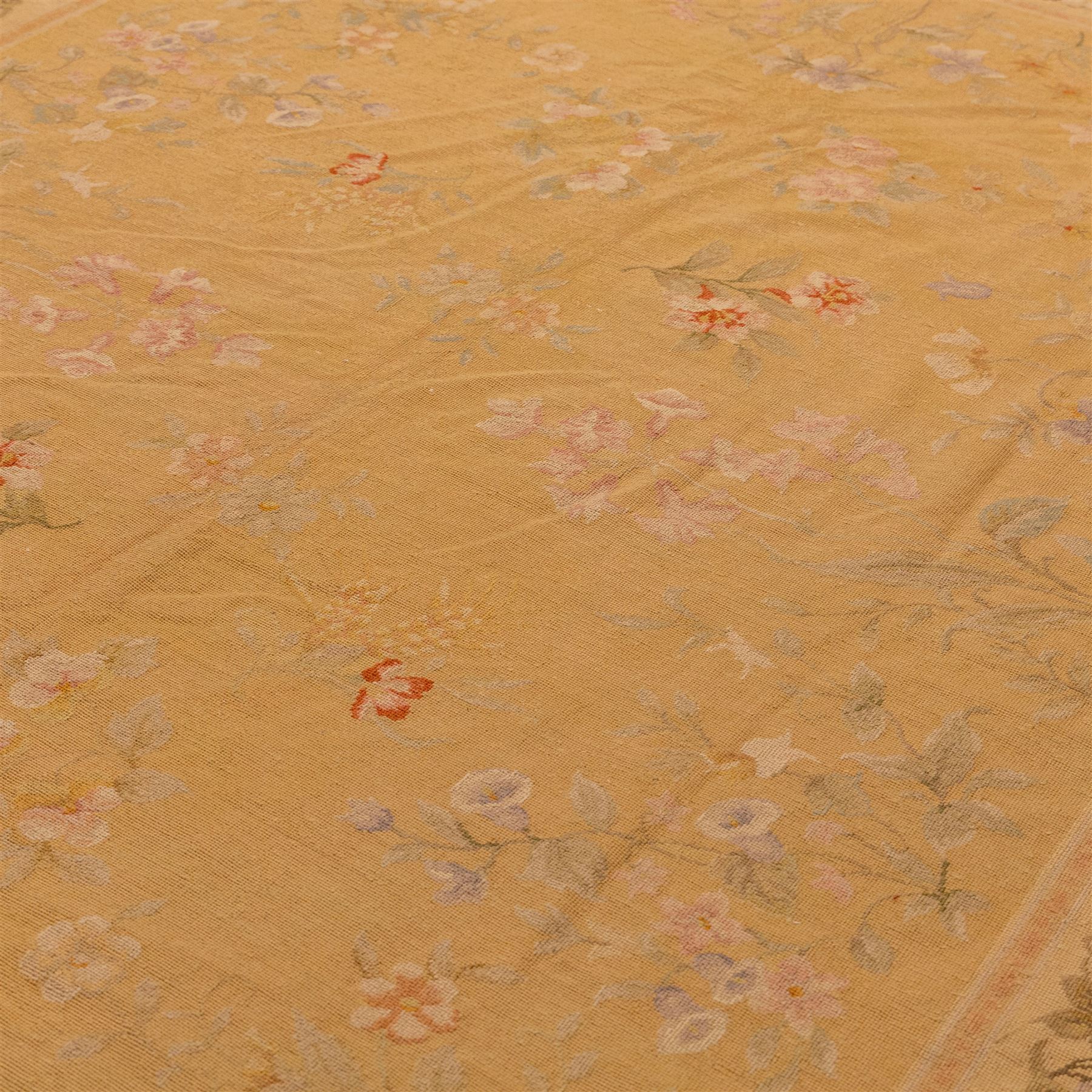 20th-century Aubusson-style woven tapestry of rectangular form with mustard yellow field decorated with scattered floral sprays in soft pastel tones of pink, cream, and muted green, within a narrow guard stripe with an outer border of trailing blossoms and foliage 