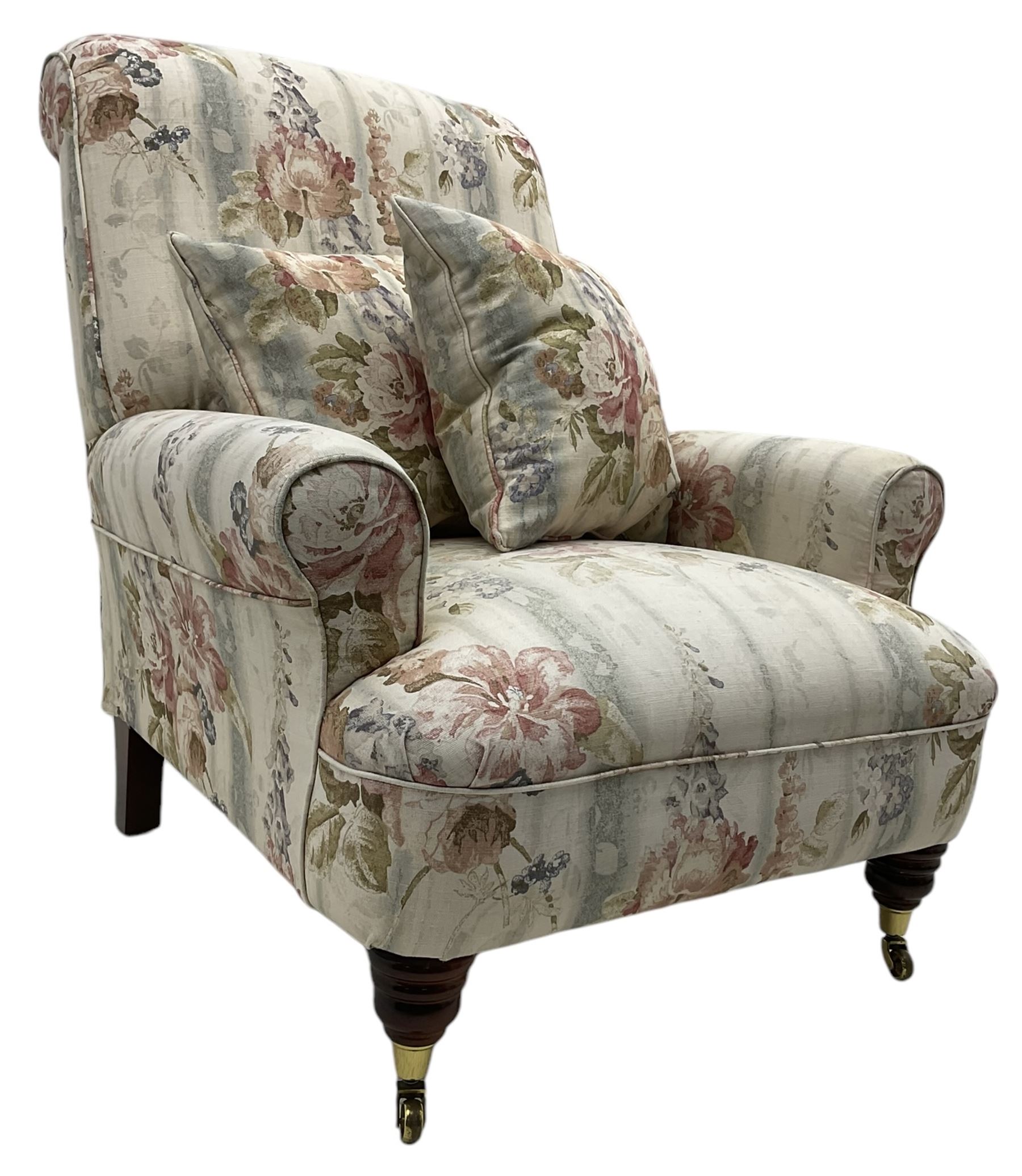 Victorian design armchair, rolled back and arms, upholstered in floral pattern fabric with two scatter cushions, on turned front feet with brass cups and castors