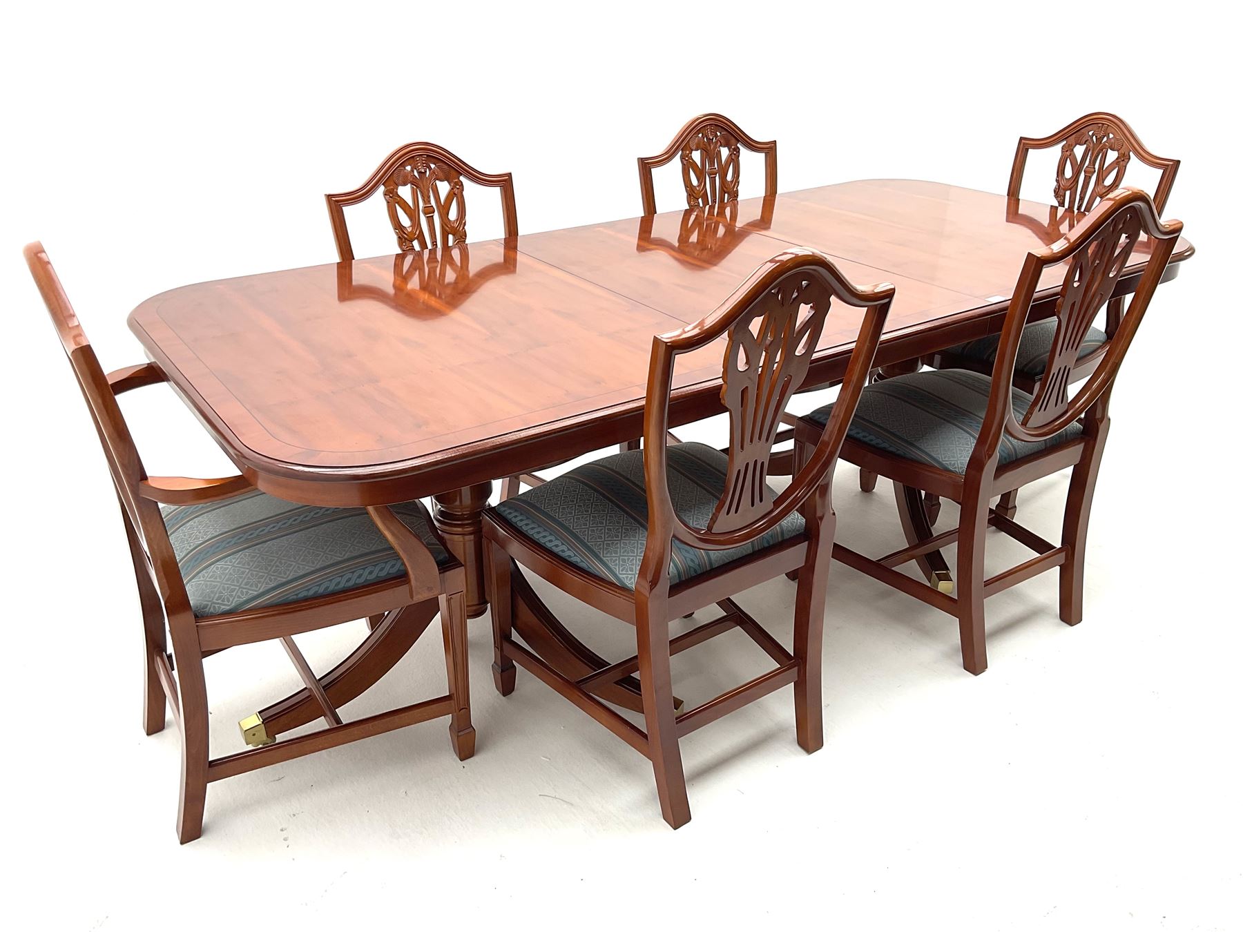 Yew wood twin pedestal extending dining table, shaped supports and brass castors (W216cm, D100cm, H77cm) and six (4+2) chairs, shaped back and upholstered in patterned fabric raised on fluted supports (W52cm)