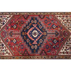 Persian Heriz crimson ground carpet, the central navy geometric medallion on a red crimson ground field, surrounded by further geometric stylised motifs and foliate designs, enclosed by multiple guard-lines  