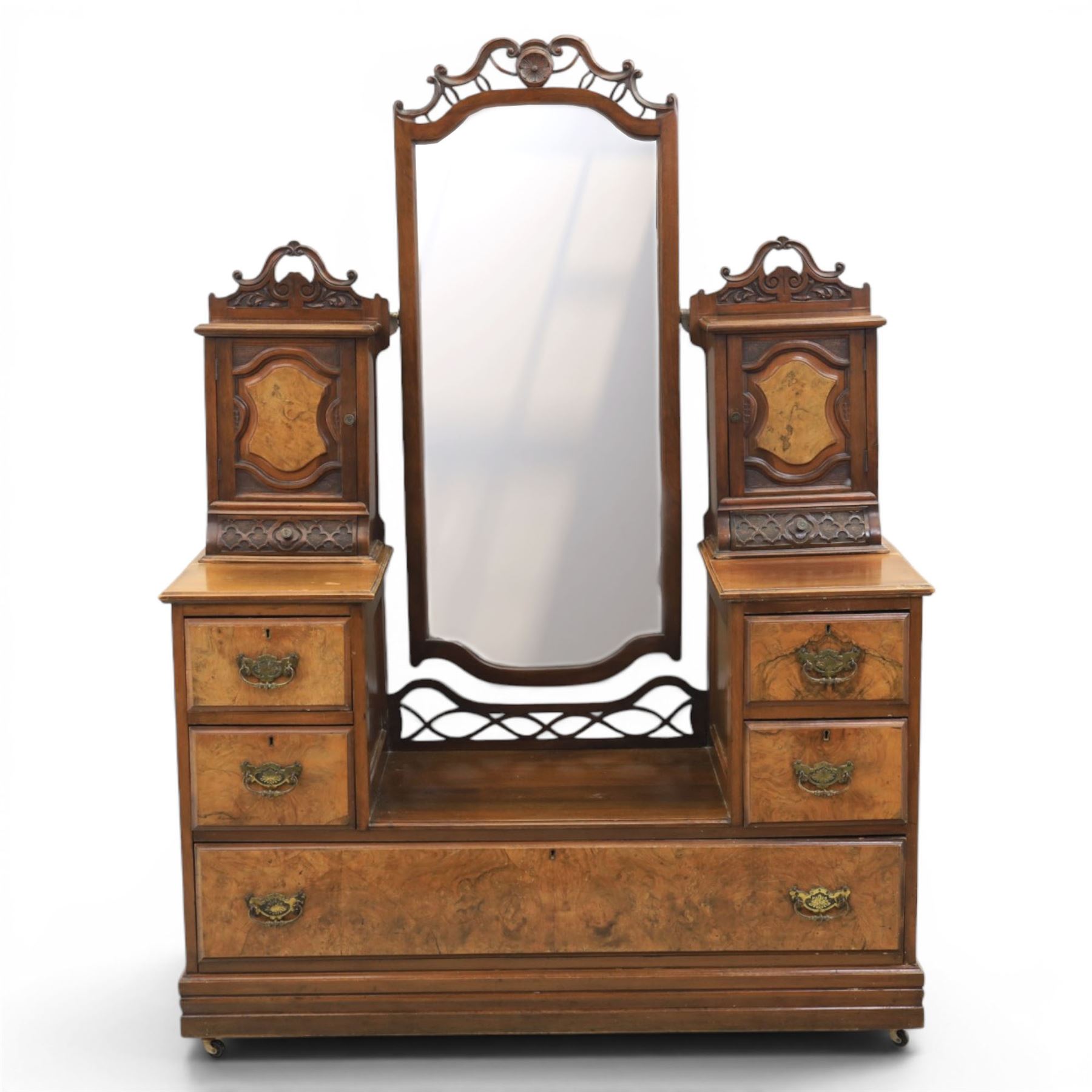 Edwardian figured walnut dressing chest, with central tilting mirror with pierced fret work, flanked by cabinet with figured walnut panelled door above a trinket drawer, with four short over a long long drawer, raised on a plinth base with castors 