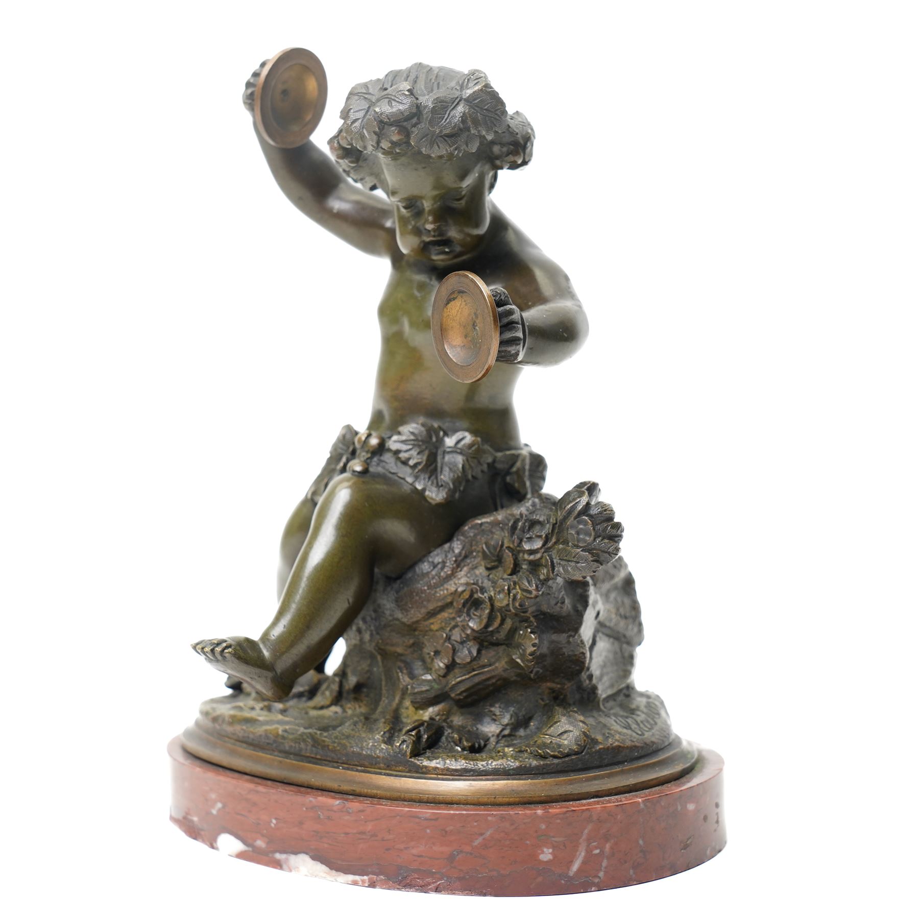 After Michel Claude Clodion (French 1738-1814): Grand Tour patinated bronze figure of a bacchic cherub, modelled dancing and playing cymbals, seated upon a naturalistic rocky base entwined with vine leaves and grapes, bearing signature, mounted on an oval red marble plinth, 19th century, W15cm H19cm