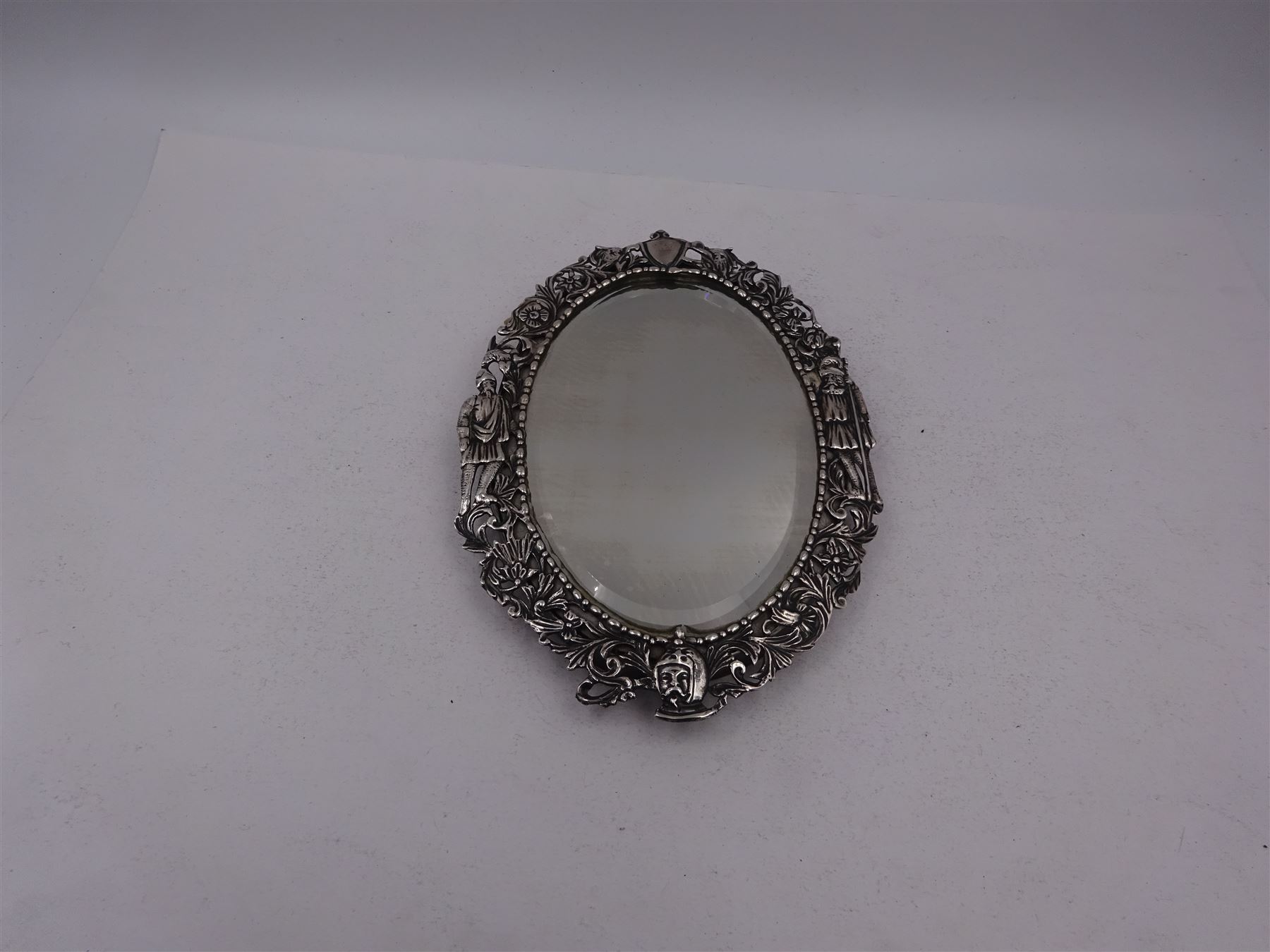 Continental silver miniature dressing table/wall mirror, of oval form with bevelled mirror plate, surrounded by a bead and dart rim, with pierced scrolling floral border with a standing cavalier to either side and the bust of a cavalier to the base, H17.7cm