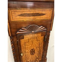 Early 19th century mahogany and oak longcase clock, the hood with scrolled pediment and central finial, stepped arch hood door enclosed by turned columns, inlaid trunk with lobe carved mount, the base inlaid with star motif, shaped apron and bracket feet, Roman enamel dial painted with farming scene, twin train movement striking on bell