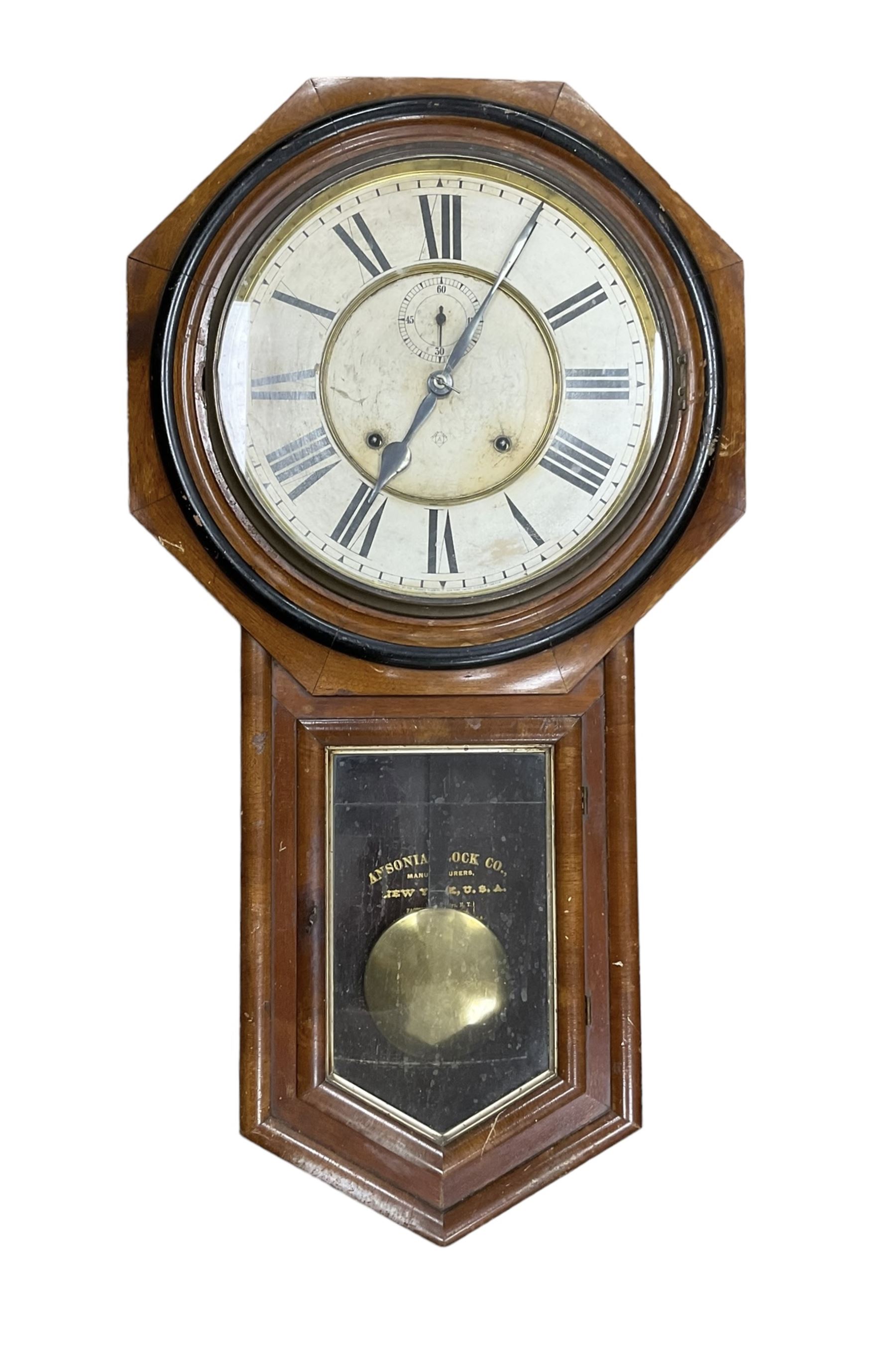 American - Late 19th century Ansonia 8-day wall clock, with a hexagonal wooden dial surround and circular spun bezel, glazed case door and visible pendulum,  two part dial with Roman numerals, minute track, spade hands and seconds dial, twin train spring driven movement striking the hours on a gong.