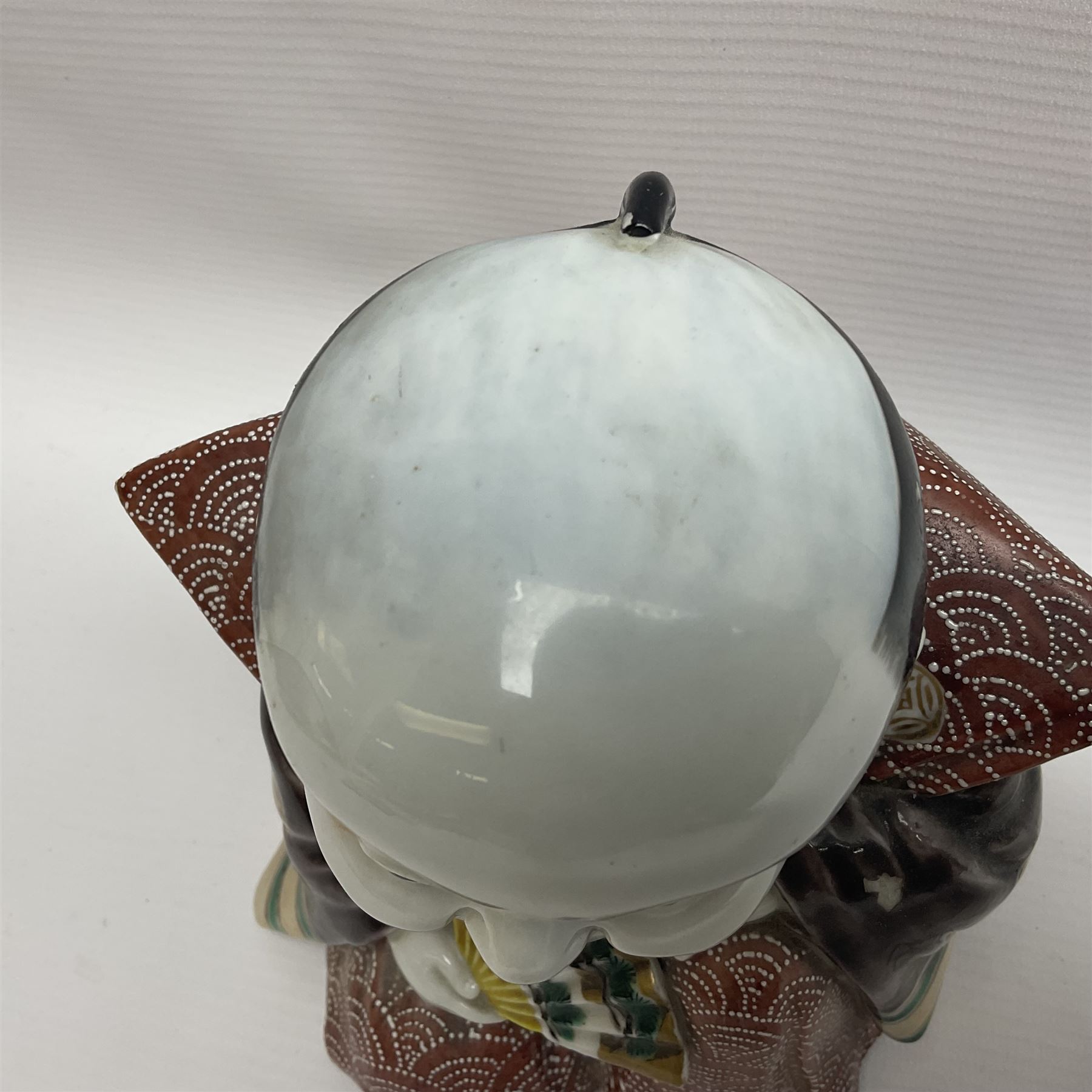 Japanese Fukusuke good fortune figure, modelled as a kneeling male figure holding a fan, dressed in traditional Samurai robes, H15.5cm