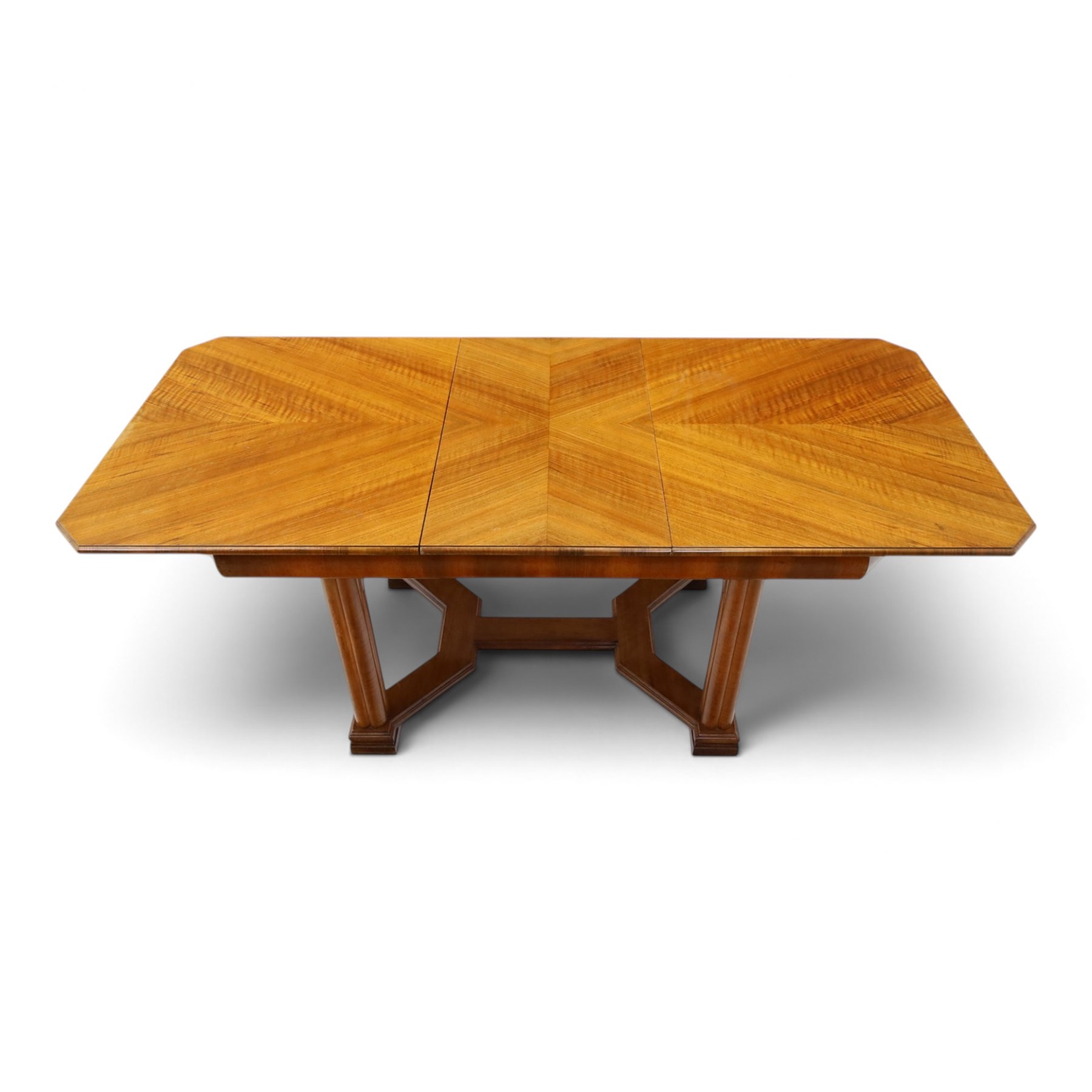 Art Deco walnut extending dining table, book-matched veneered shaped top, raised on cluster-column supports, united by stretchers, additional leaf extends to 185cm  