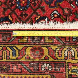 Hamadan hand-knotted rug, red field with small central floral medallion and dense repeating geometric motifs in dark blue, cream and green tones, within multiple patterned borders
