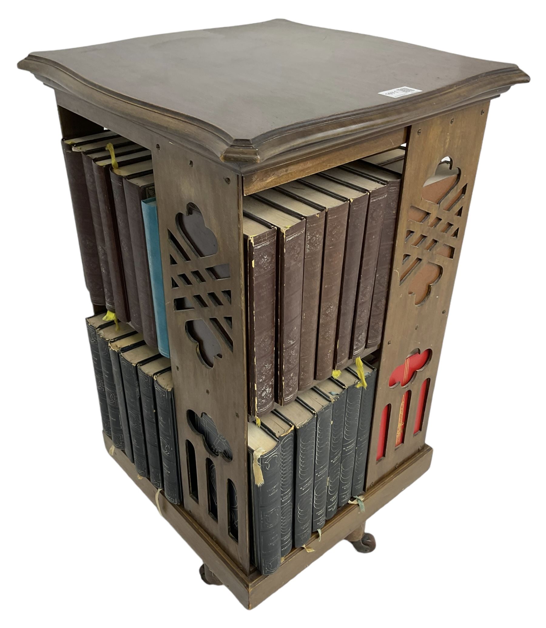 Late Victorian revolving bookcase, shaped square top over fretwork supports of geometric and arcade design, on a swivel action base with ceramic castors