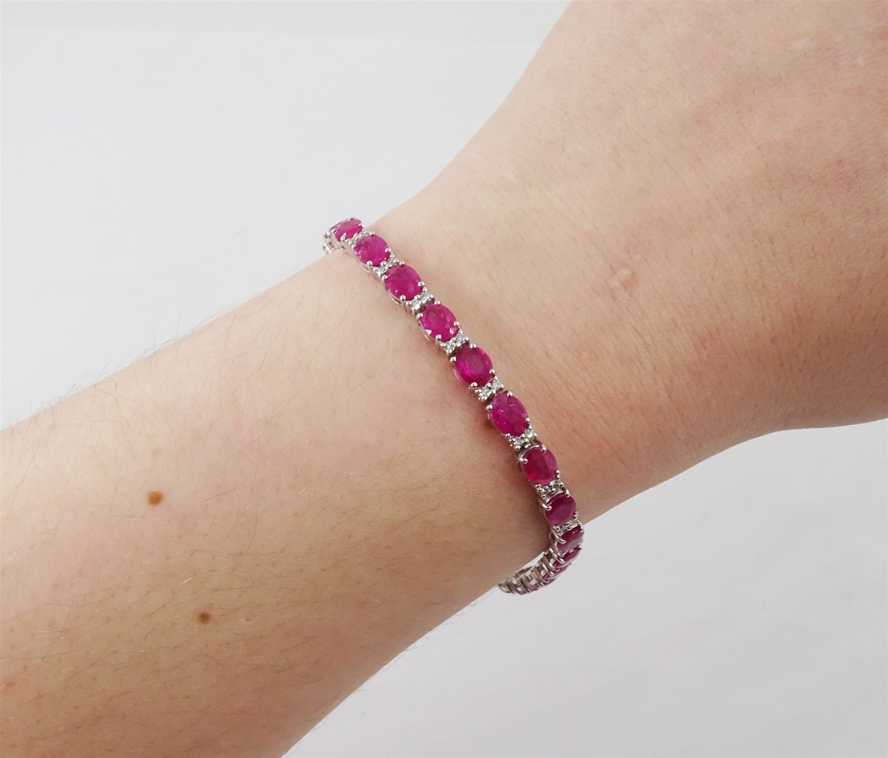 18ct white gold ruby and diamond bracelet, twenty-six oval cut rubies, each spaced by two round brilliant cut diamonds, hallmarked, total ruby weight approx 9.40 carat, total diamond weight 0.50 carat