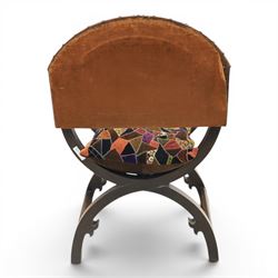 Early 20th century mahogany Savonarola chair, arched leather back with brass studwork, curved open arms with incised geometric decoration, loose patchwork velvet cushion seat, X-frame supports united by circular side rails, on scrolled feet