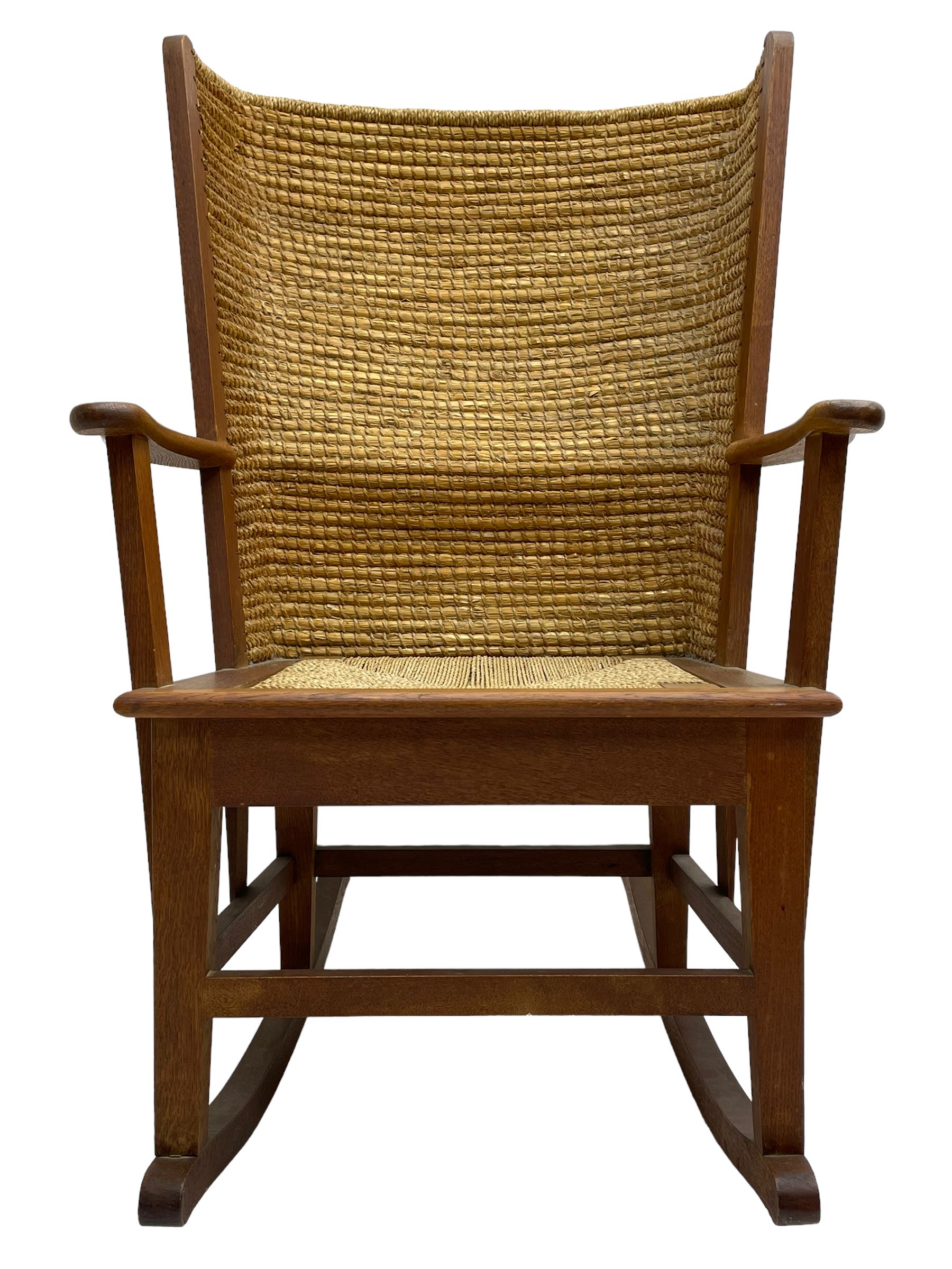 Reynold Eunson (1932–1978) for David Munro Kirkness, Kirkwall, Orkney - oak framed Orkney rocking chair, woven straw curved back, drop-in rush seat, the arm terminals with carved end scroll, on square tapering supports joined by plain stretchers, the front rail inscribed with makers marks
